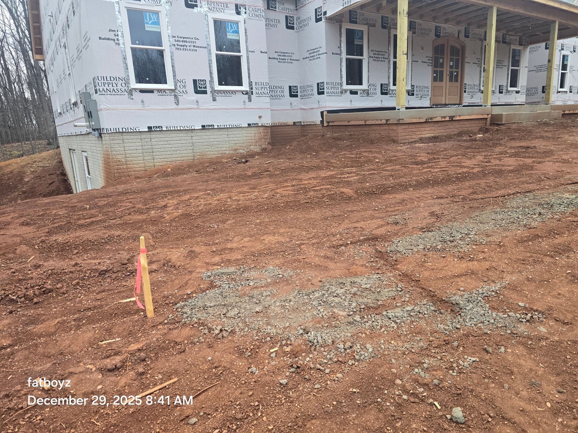 Construction site with red dirt grading in front of a house under renovation, with a yellow stake in the foreground