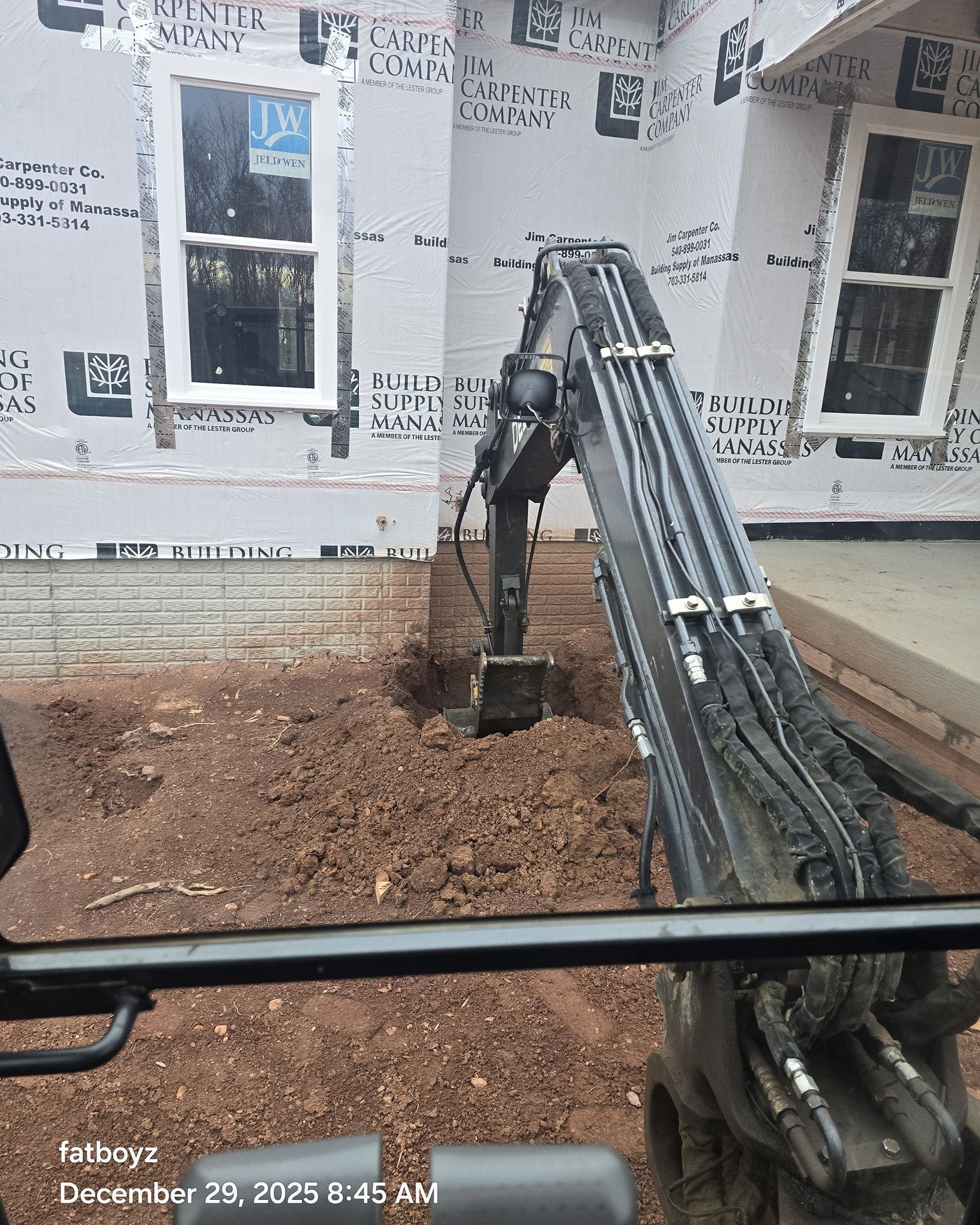 Excavator arm at a house under construction, with wood chips and unfinished exterior walls.