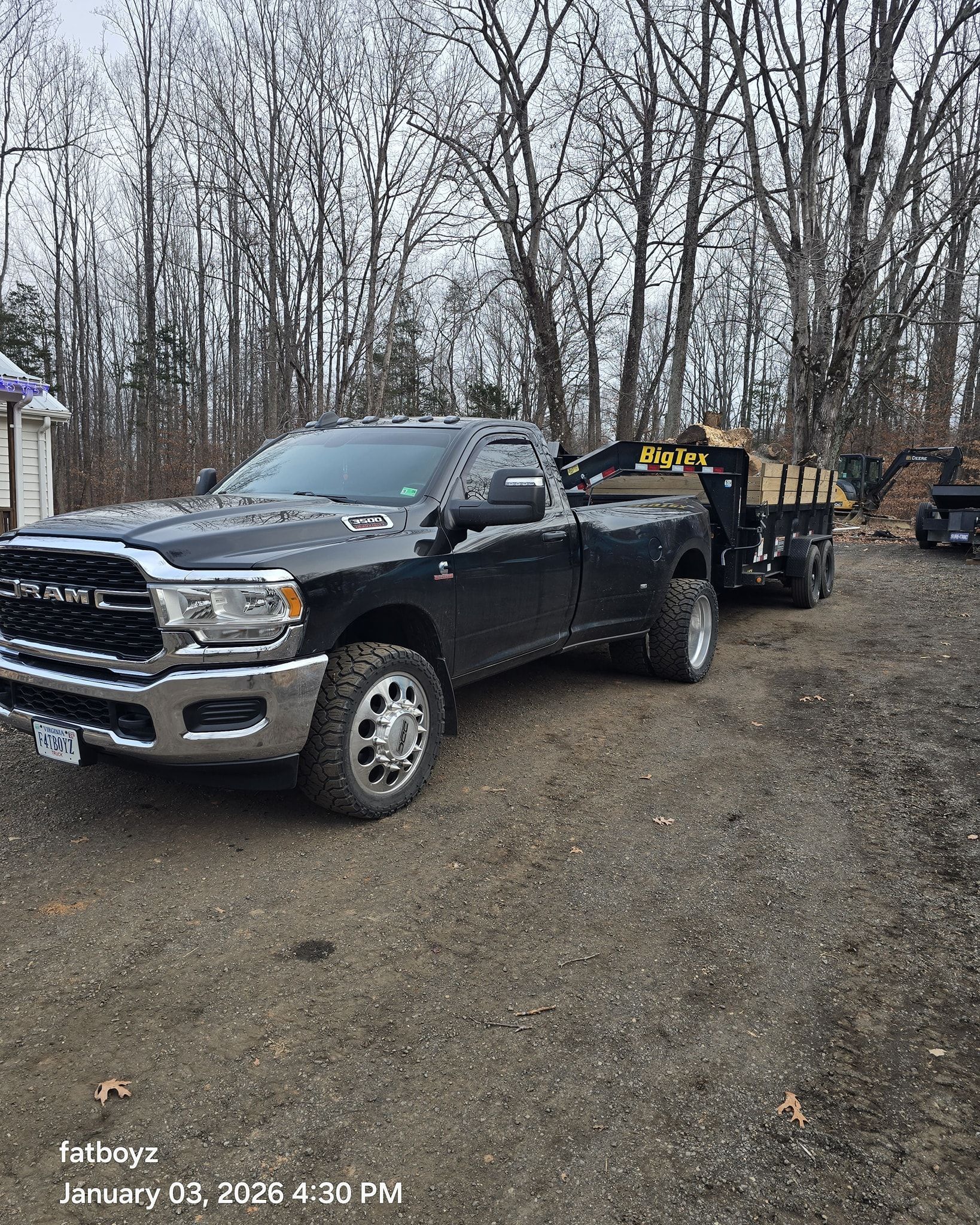 Black pickup truck towing a trailer on a gravel lot with leafless trees in the background