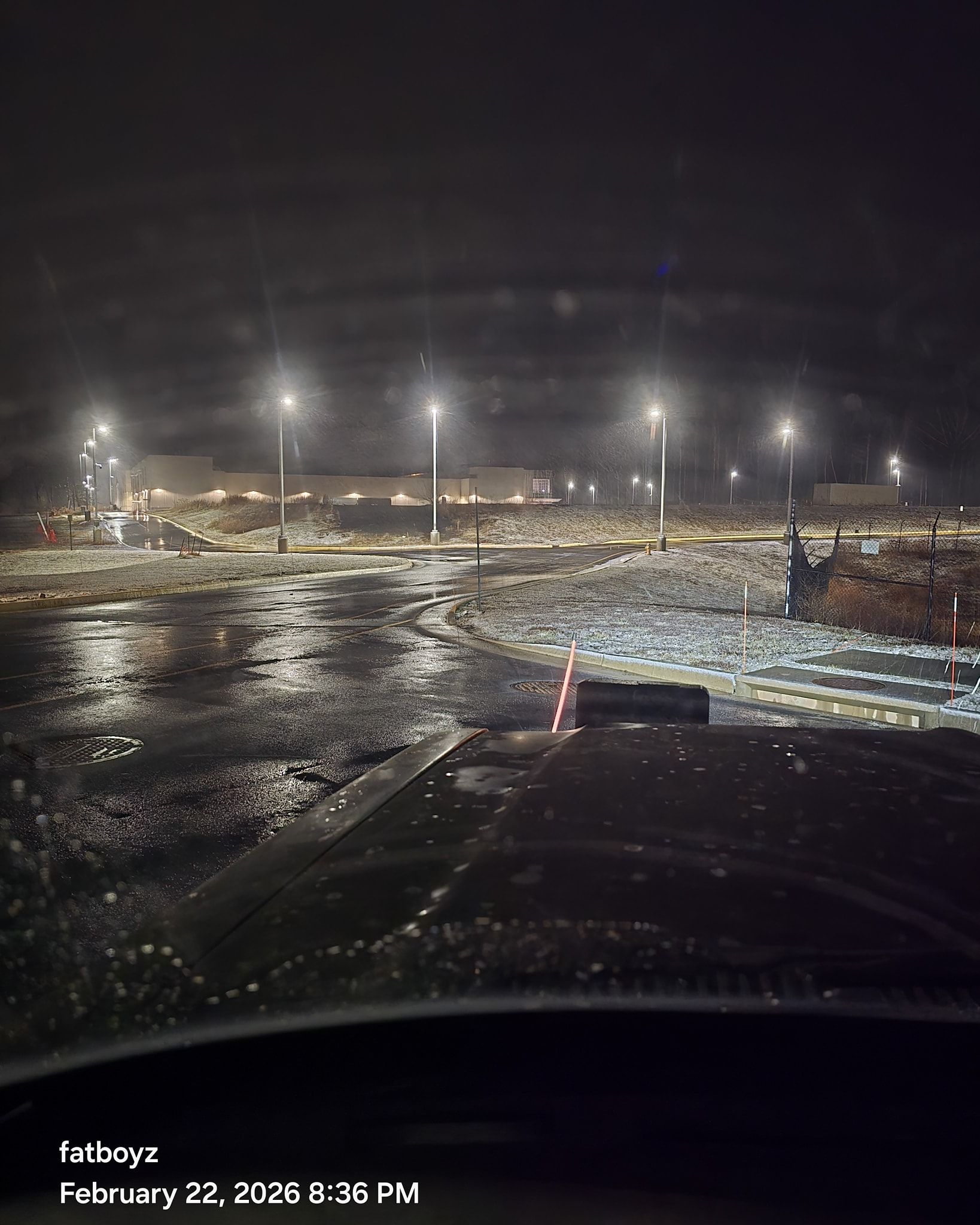 Rainy nighttime parking lot with bright lights and wet pavement reflecting glare