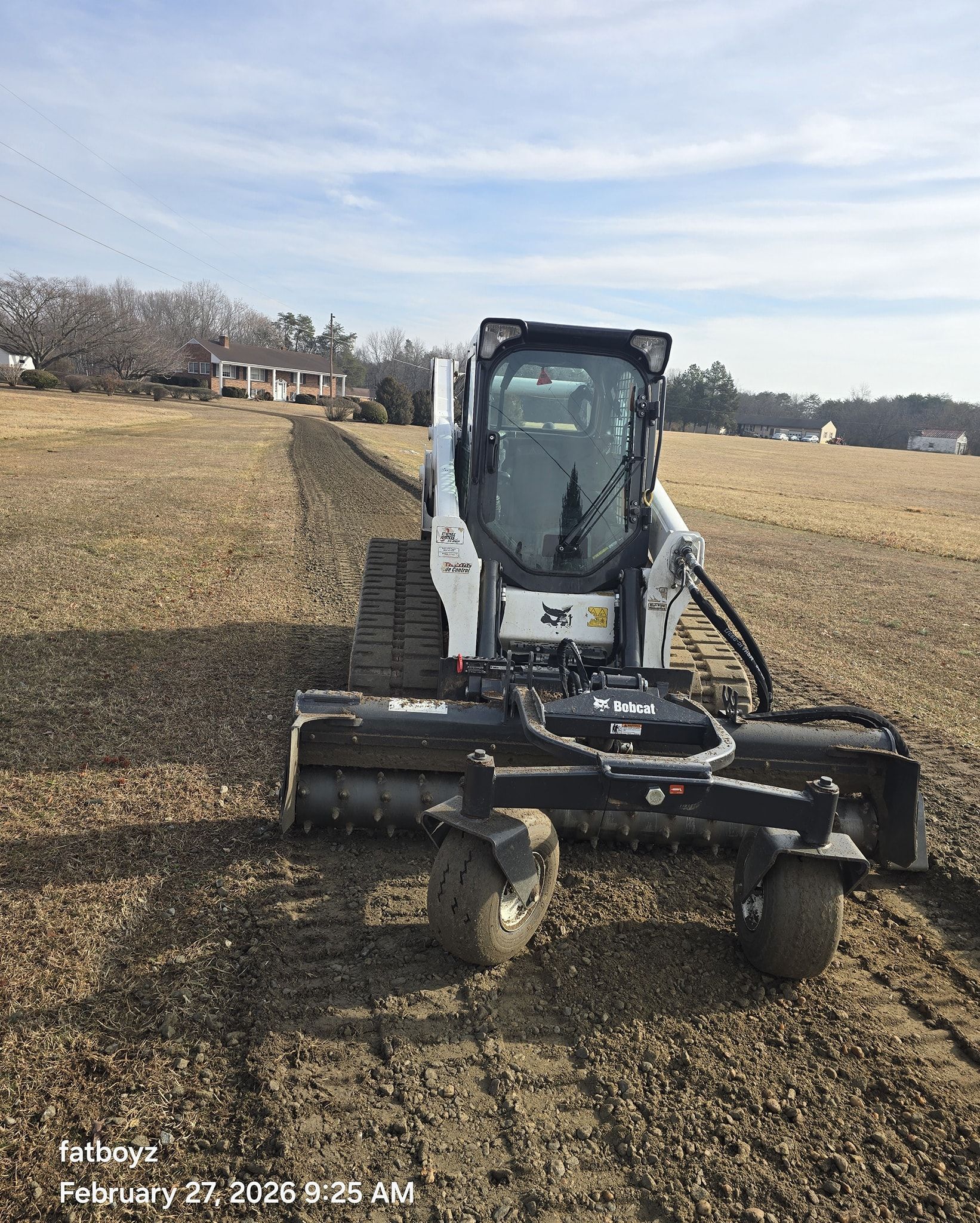 Compact excavator mowing a grassy field under a cloudy sky