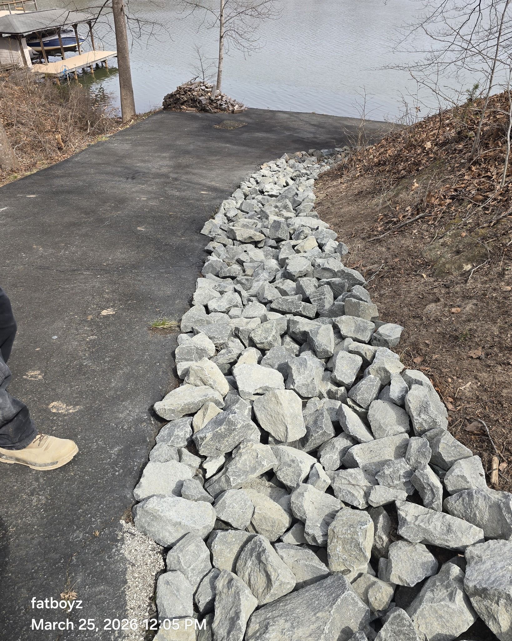 Rock-lined path leading to a calm pond, with a blacktop walkway and mulch on the side.