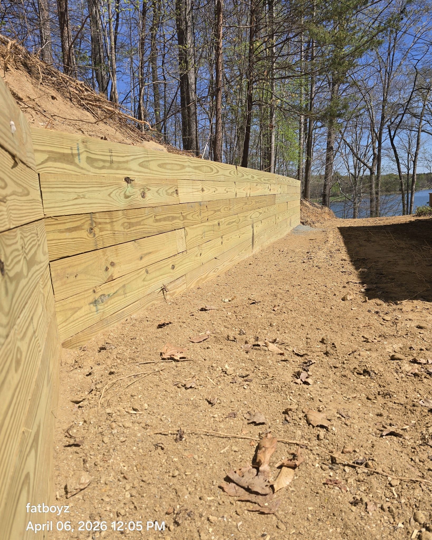 Wooden retaining wall along a dirt trail in a wooded area beside a lake