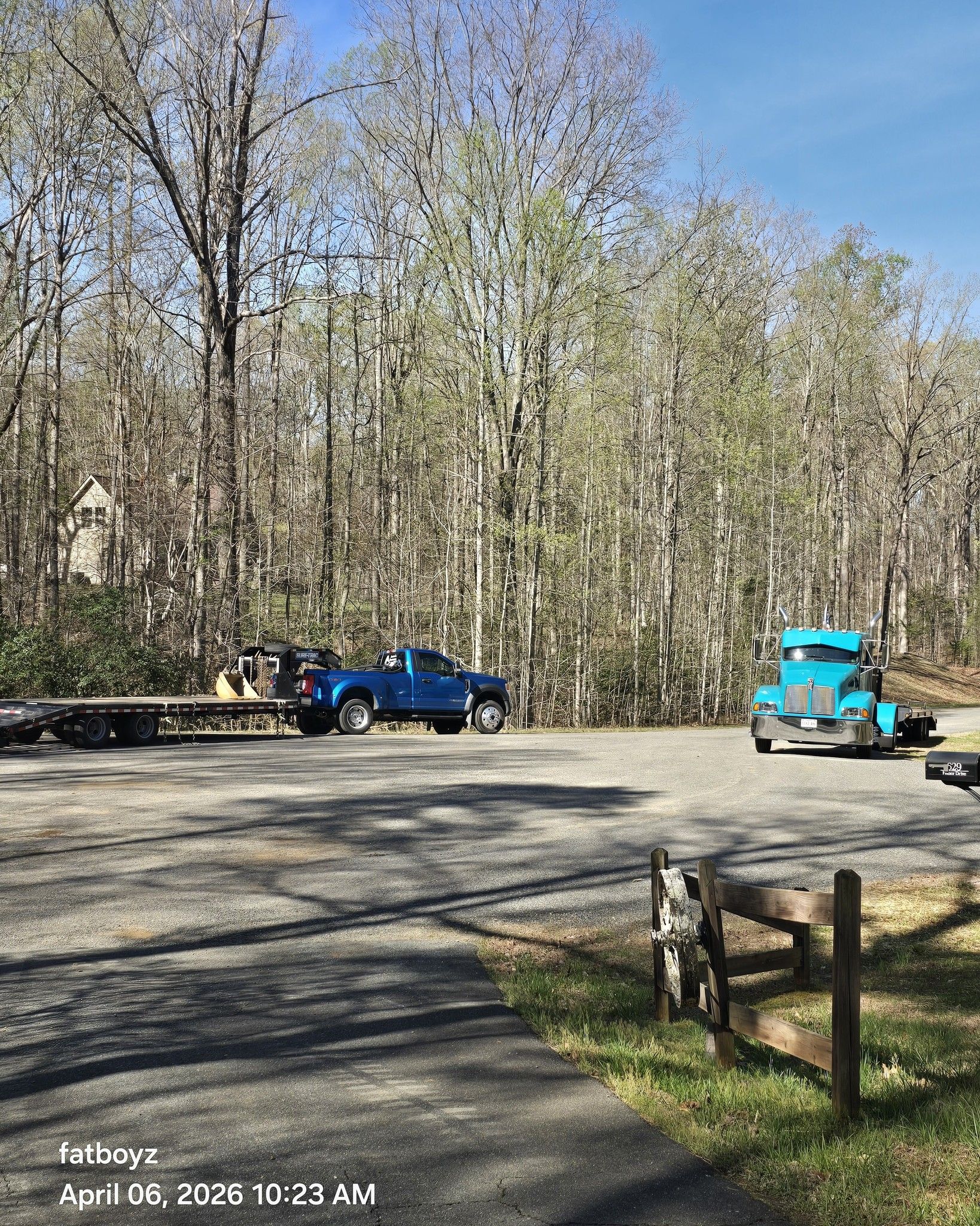 Blue pickup and turquoise vintage truck parked on a gravel lot beside tall trees on a sunny day