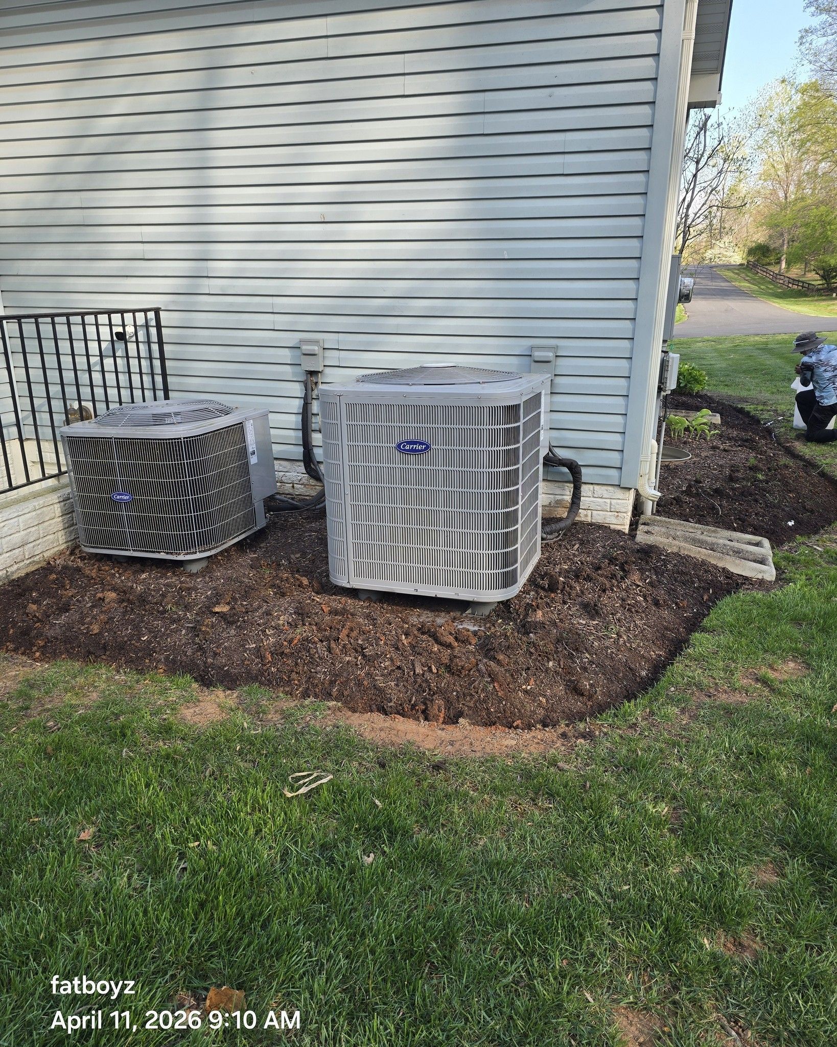 Two outdoor HVAC units beside a house on a mulched bed with white siding.