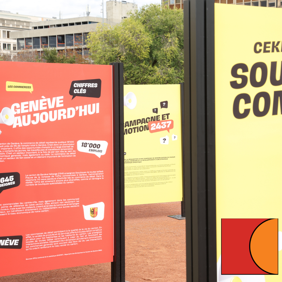 Exposition extérieure d'affiches françaises colorées sur des supports, dont une affiche rouge « Genève aujourd'hui » et une affiche jaune dans un cadre évoquant un parc.