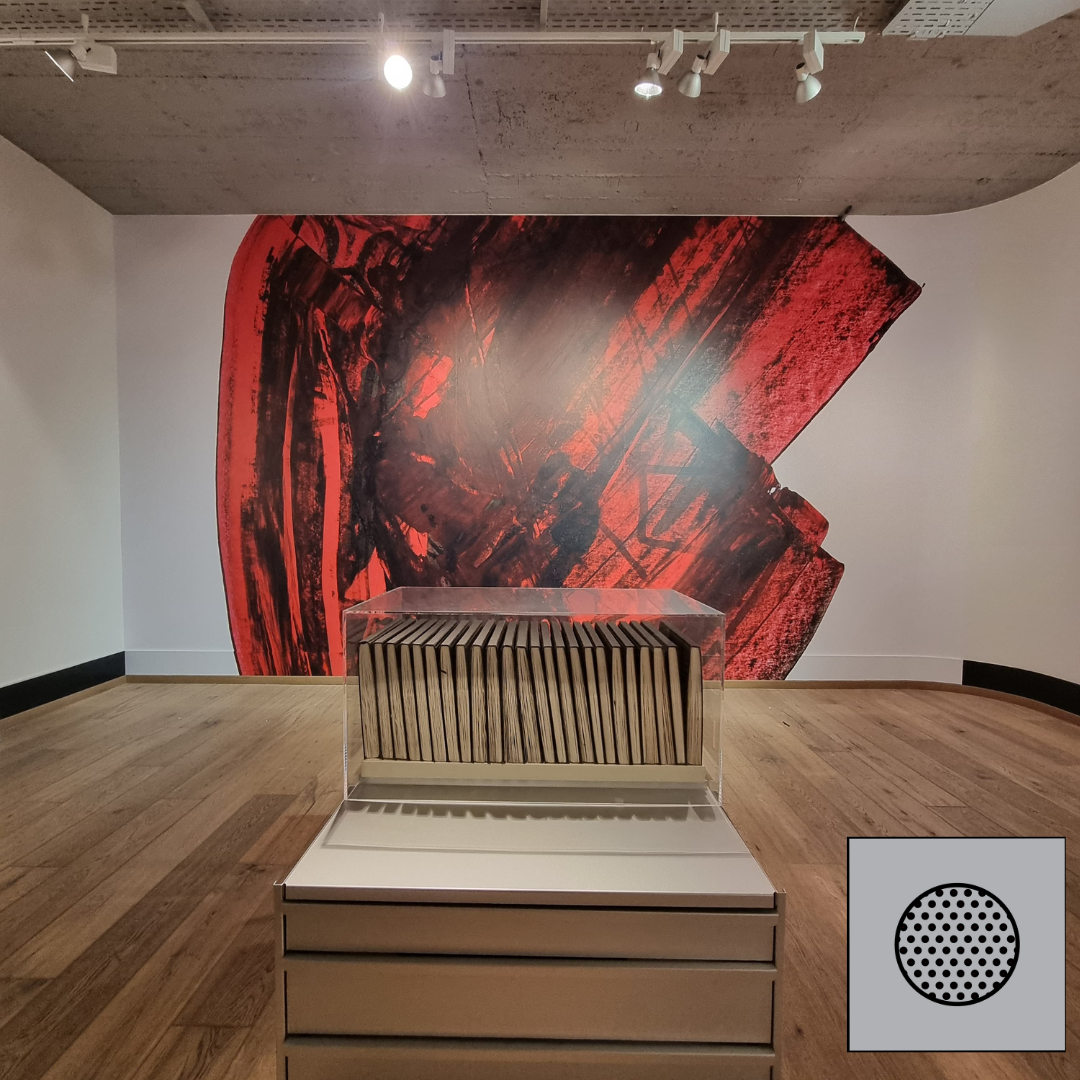 Galerie d'art avec une fresque murale abstraite rouge et noire et une sculpture en bois rayée sur un piédestal au centre.