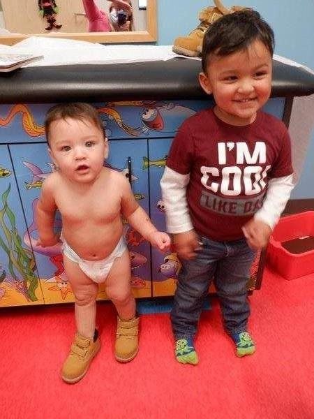 Two young children, one in a diaper, the other in a shirt and jeans, wearing brown boots.
