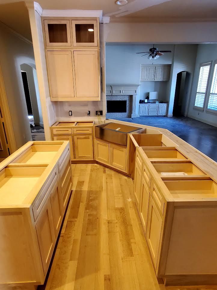 Kitchen under construction, with unfinished wooden cabinets and island on light wood floor.