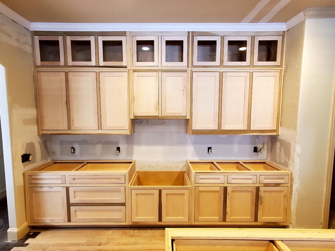 Unfinished kitchen cabinets in various sizes, installed on a wall with drywall and trim, prior to painting.