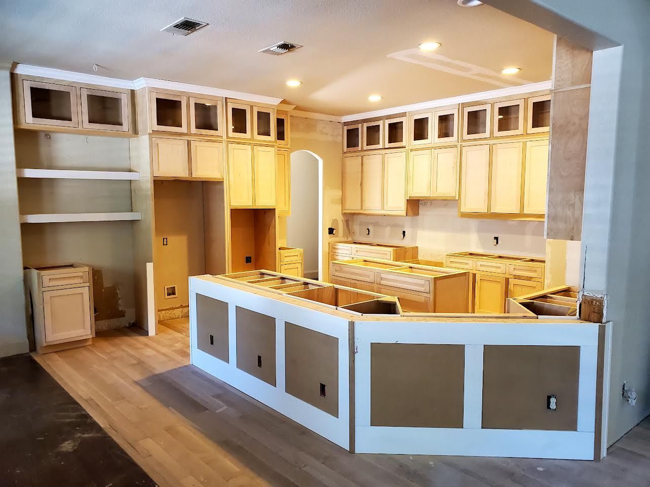 Kitchen renovation: unfinished cabinets, island, and shelving with light wood flooring.