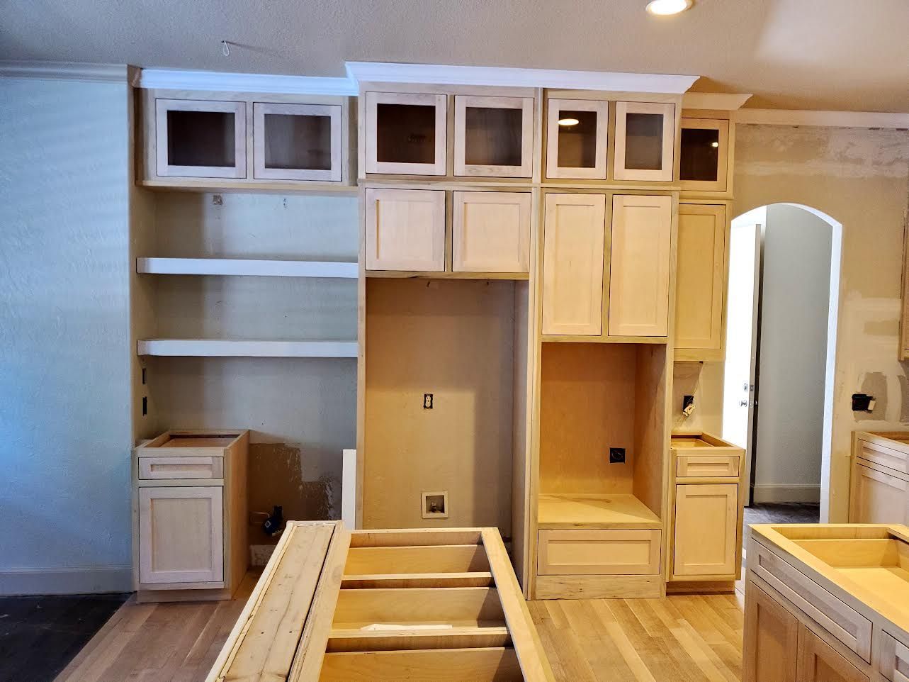 Kitchen cabinets under construction, unfinished wood, with open shelving, an appliance nook, and an island.
