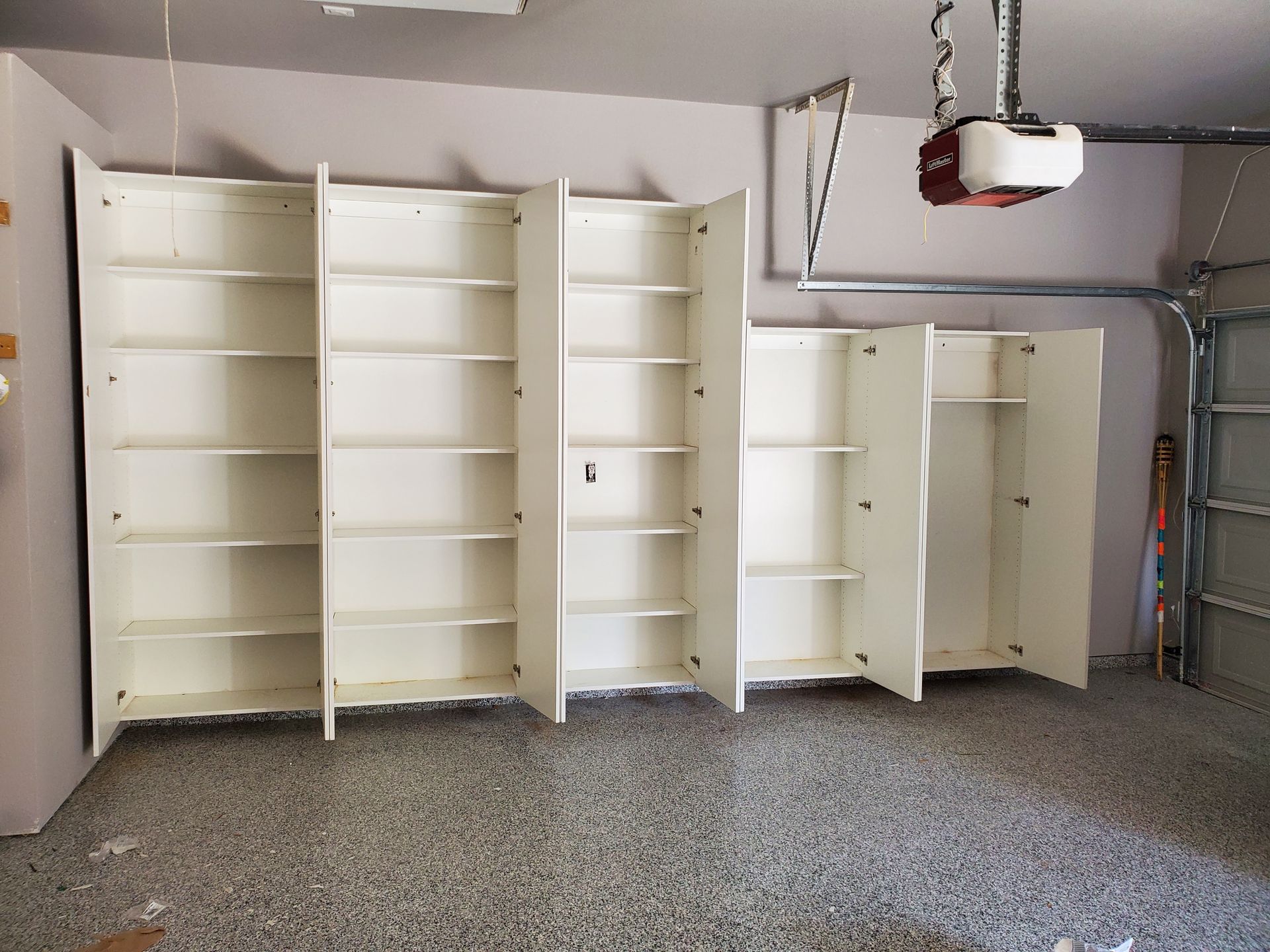 White cabinets with open shelves in a garage with a speckled floor.