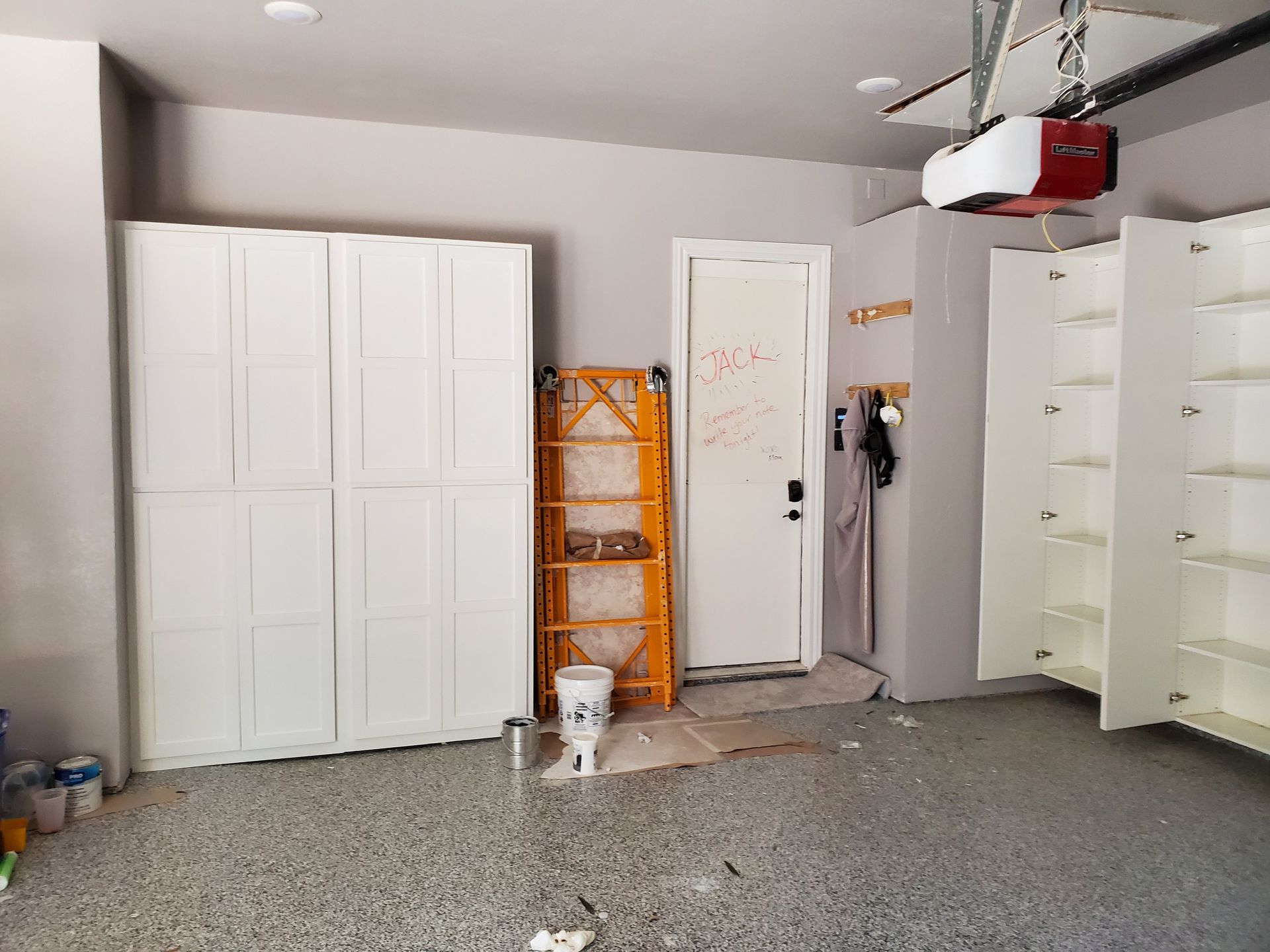 Garage interior with white cabinets, a yellow ladder, and a door, grey walls, and epoxy floor.