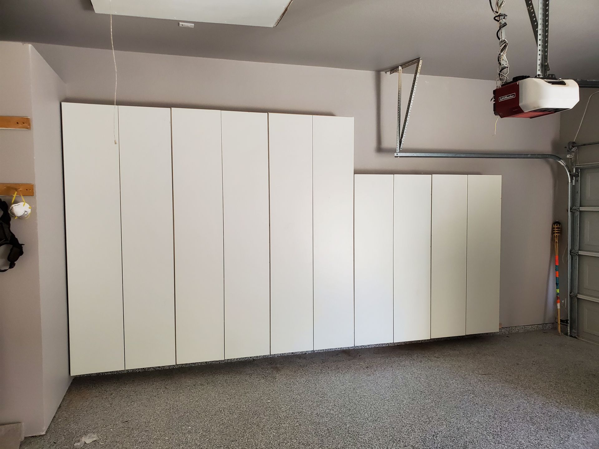 White storage cabinets mounted on a garage wall, near a garage door and opener.