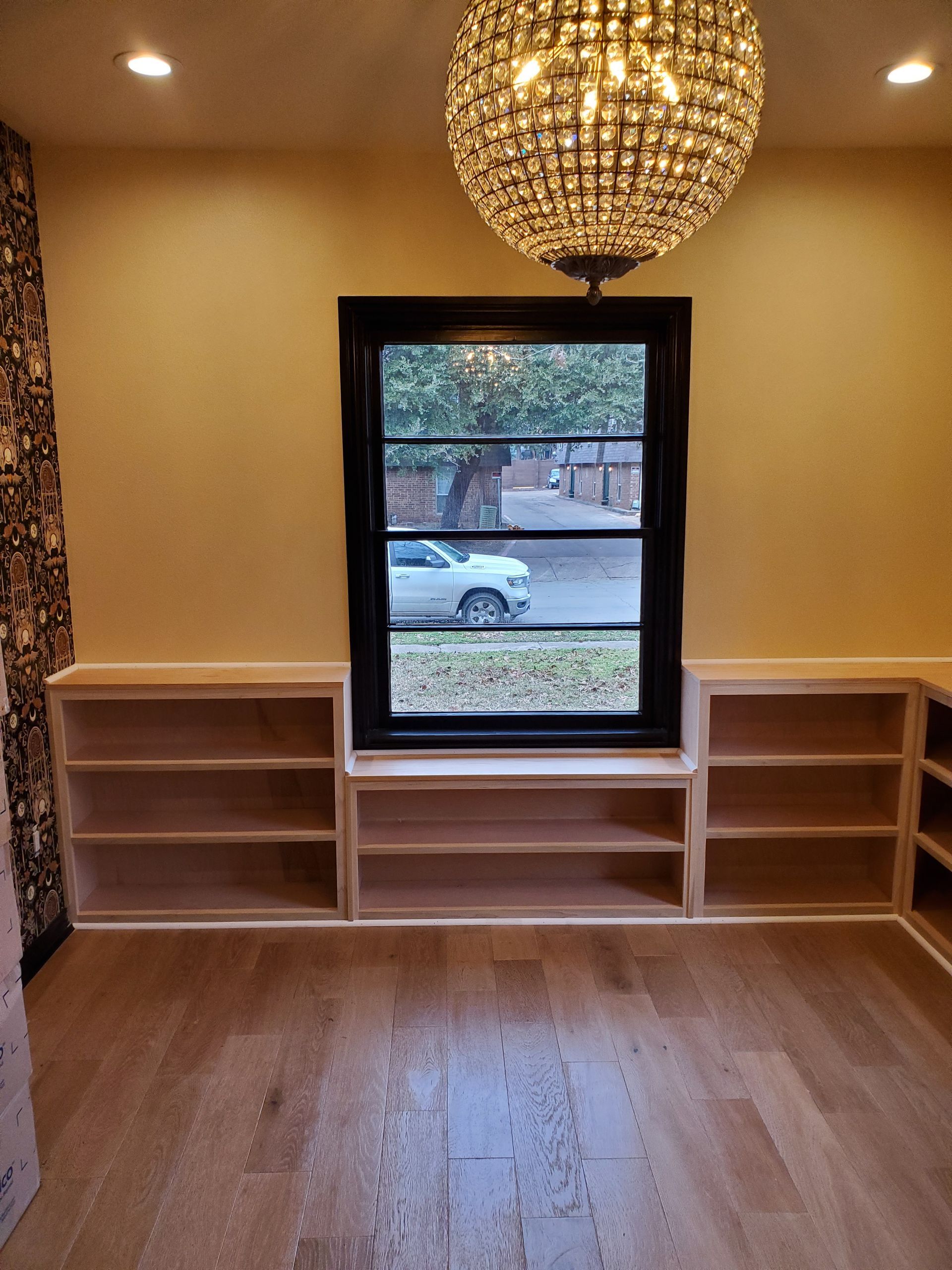 Room with wooden floors, window with black trim, built-in bookshelves, and crystal chandelier.