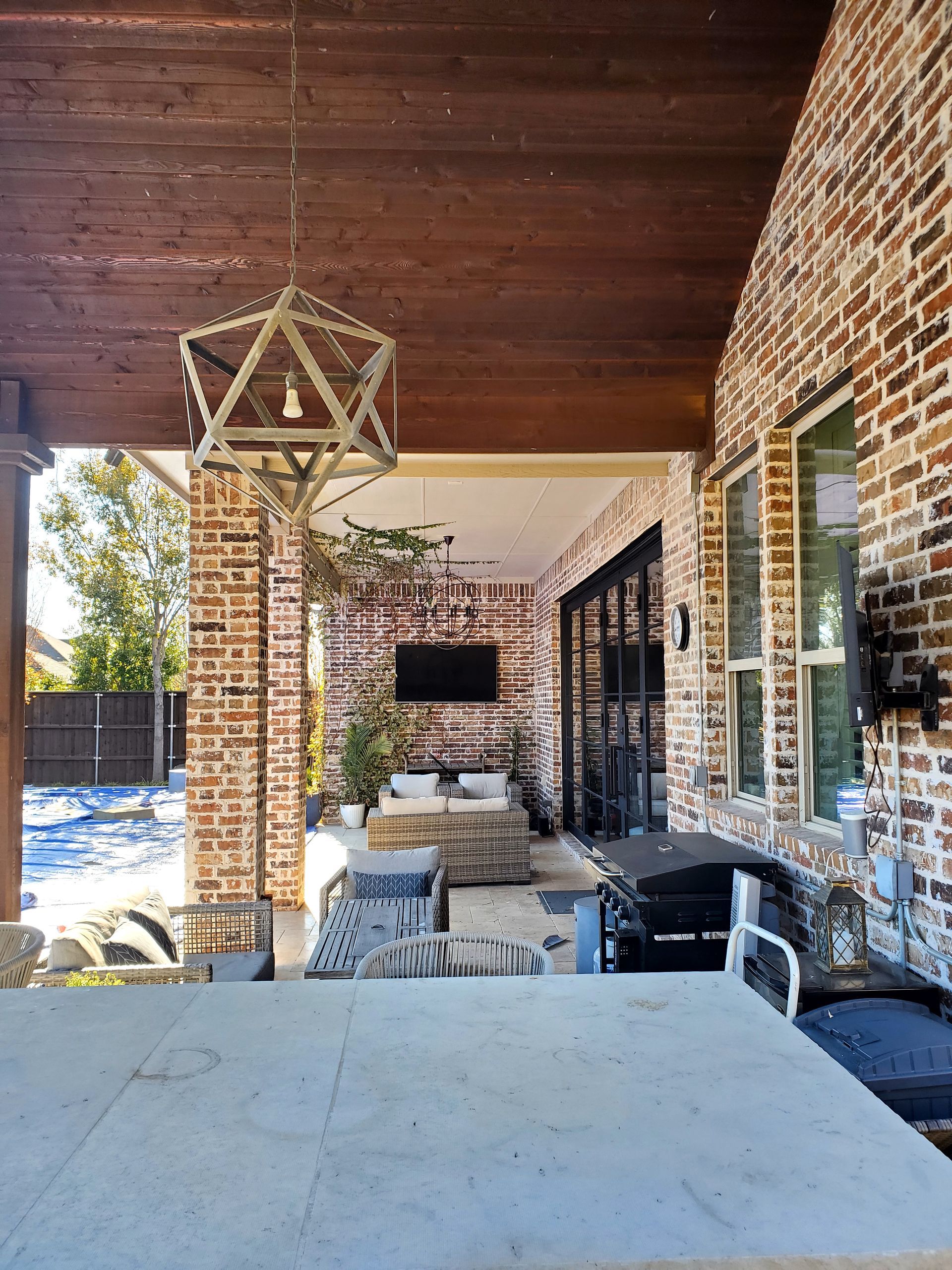 Outdoor patio with brick walls, wooden beams, a TV, and seating.