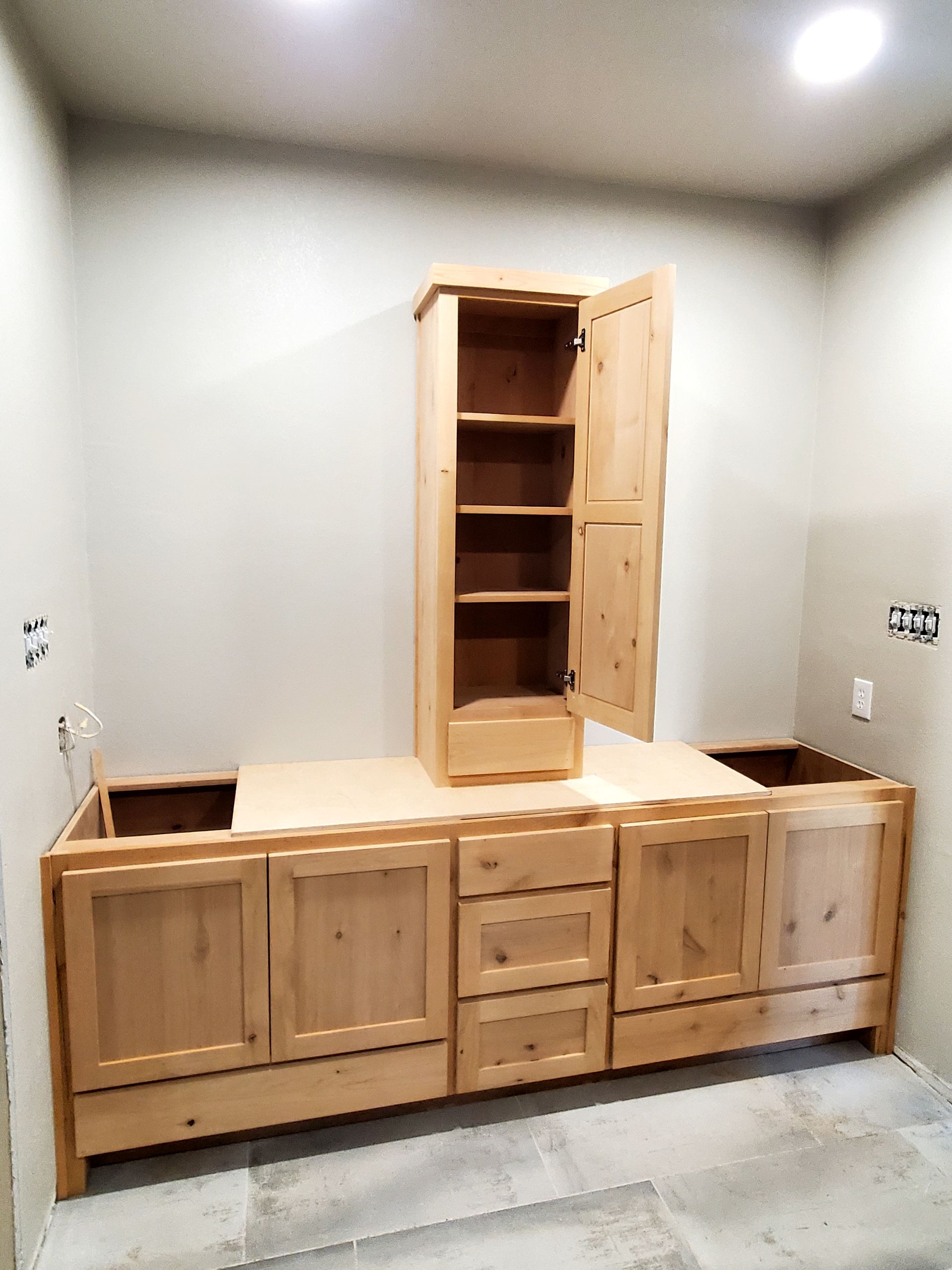 Wooden bathroom cabinets being installed. Tall cabinet with open door sits on countertop base.