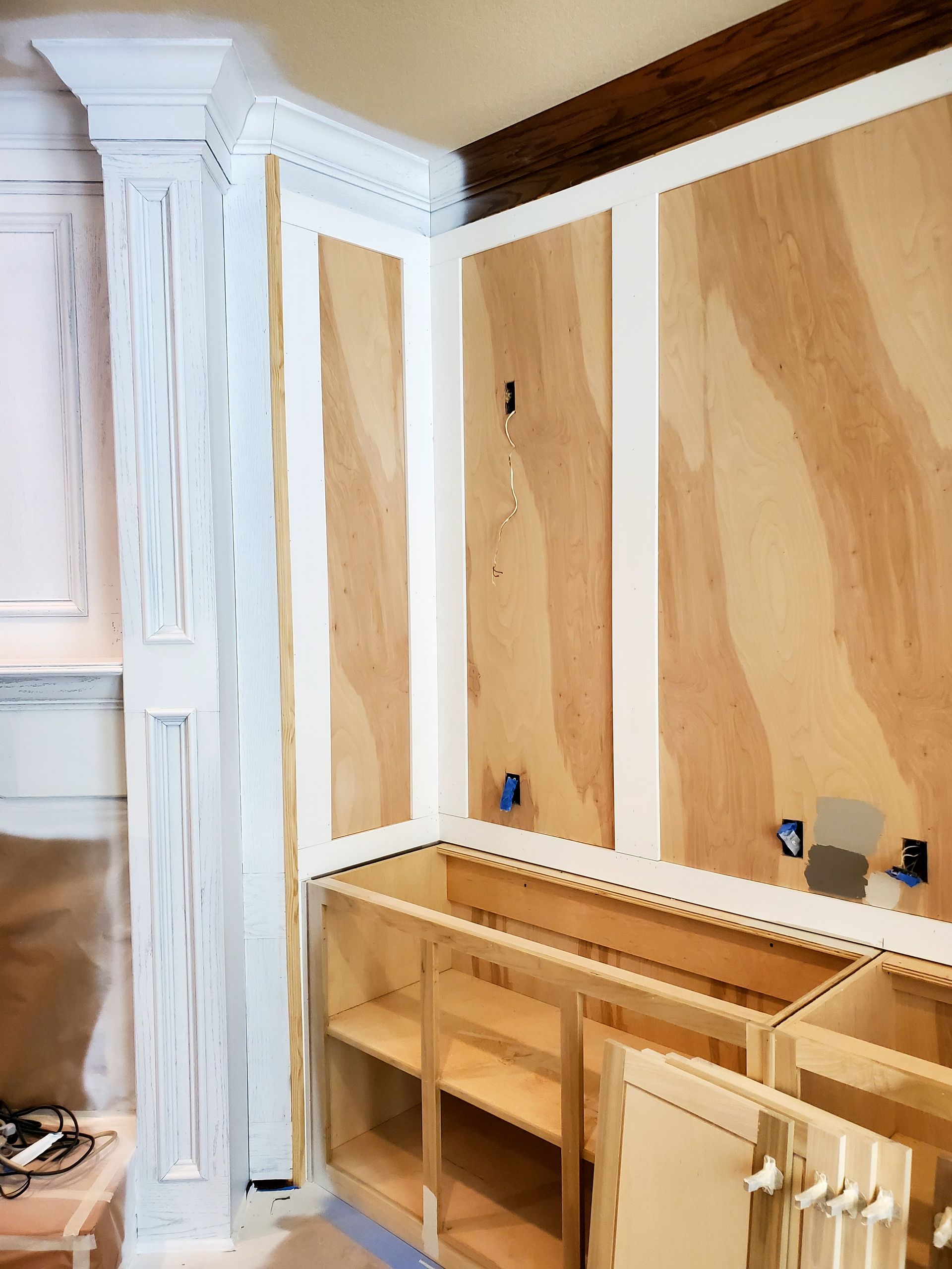 Kitchen under construction, with wooden wall panels and cabinets, white trim, and electrical outlets.