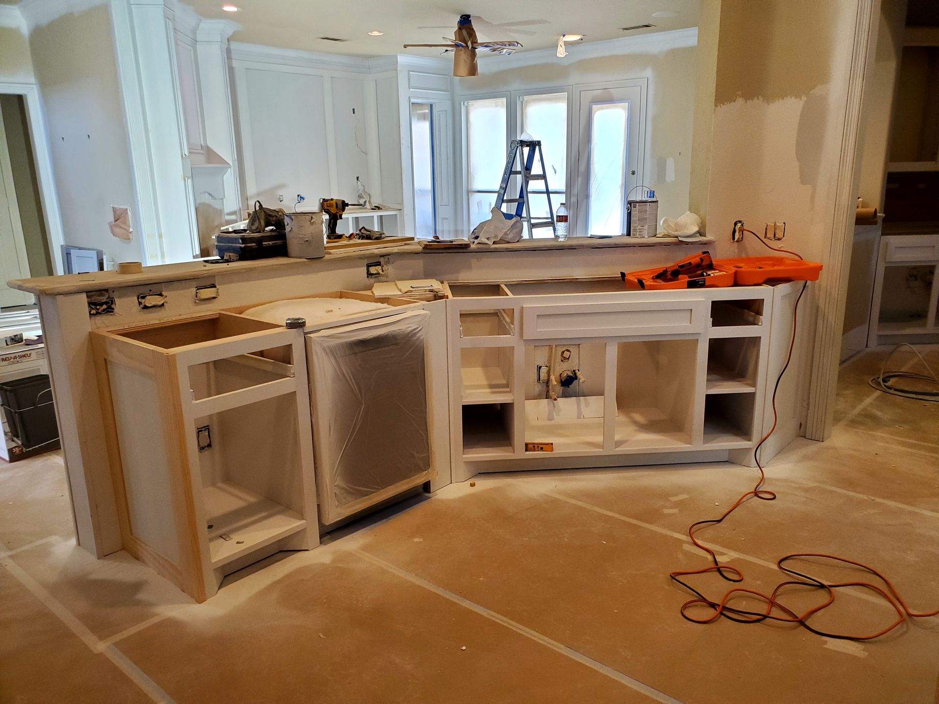 Kitchen under renovation, unfinished cabinets, countertop, tools, debris on the floor, windows in the background.