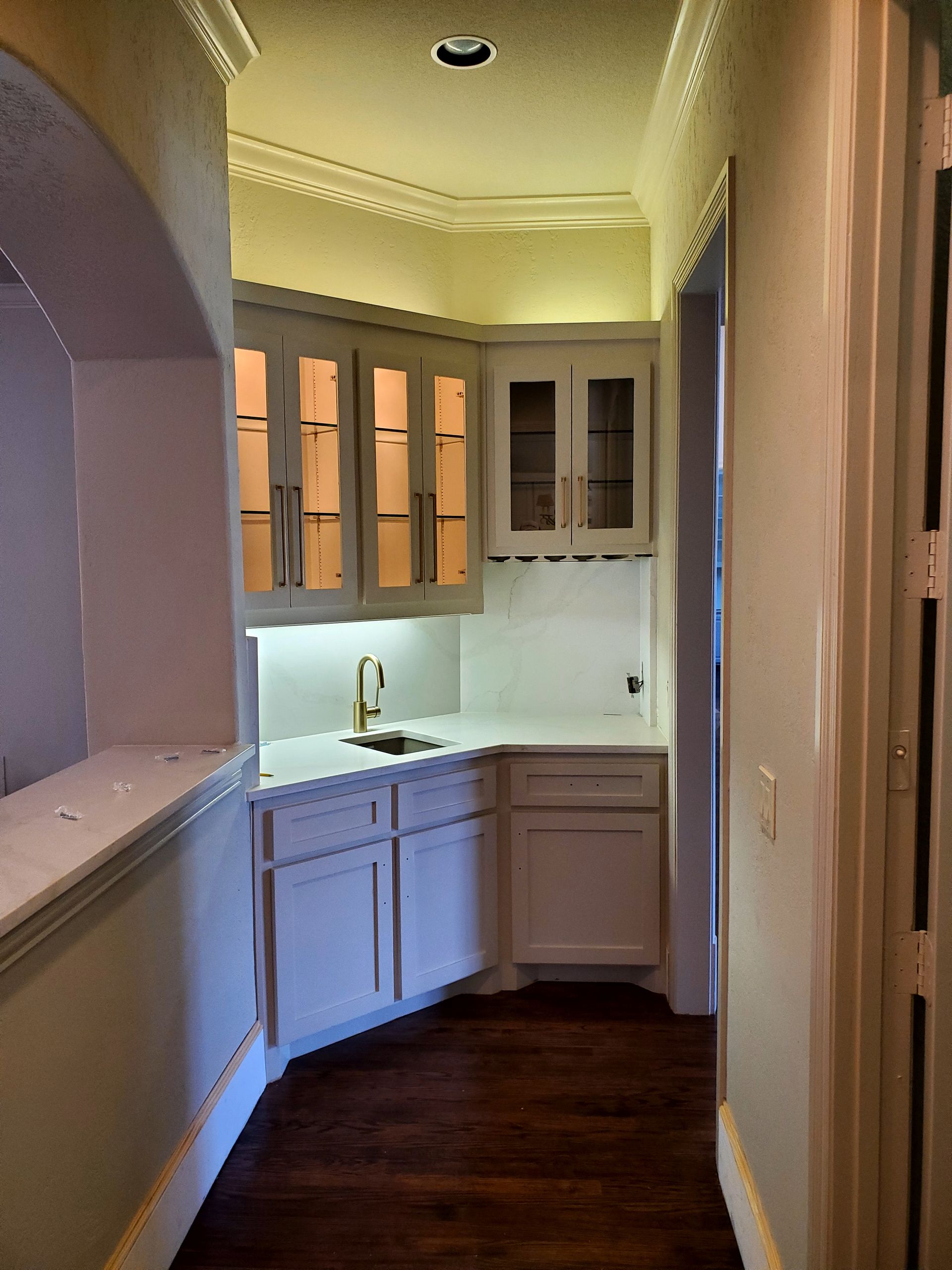White built-in bar in hallway, with cabinets, sink, and countertop. Dark wood floor.