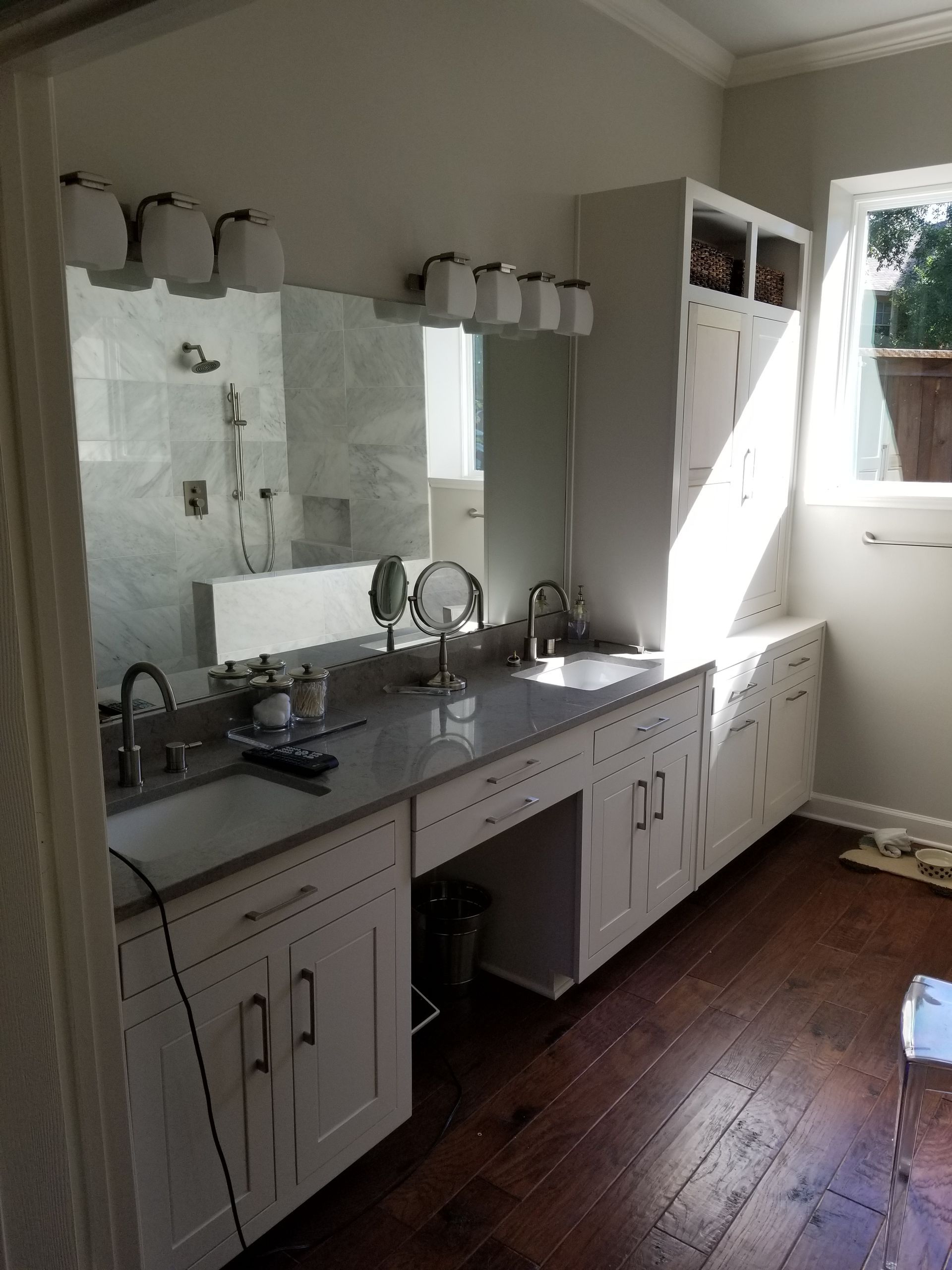 Bathroom with double sinks, white cabinets, gray countertop, large mirror, and wood flooring.