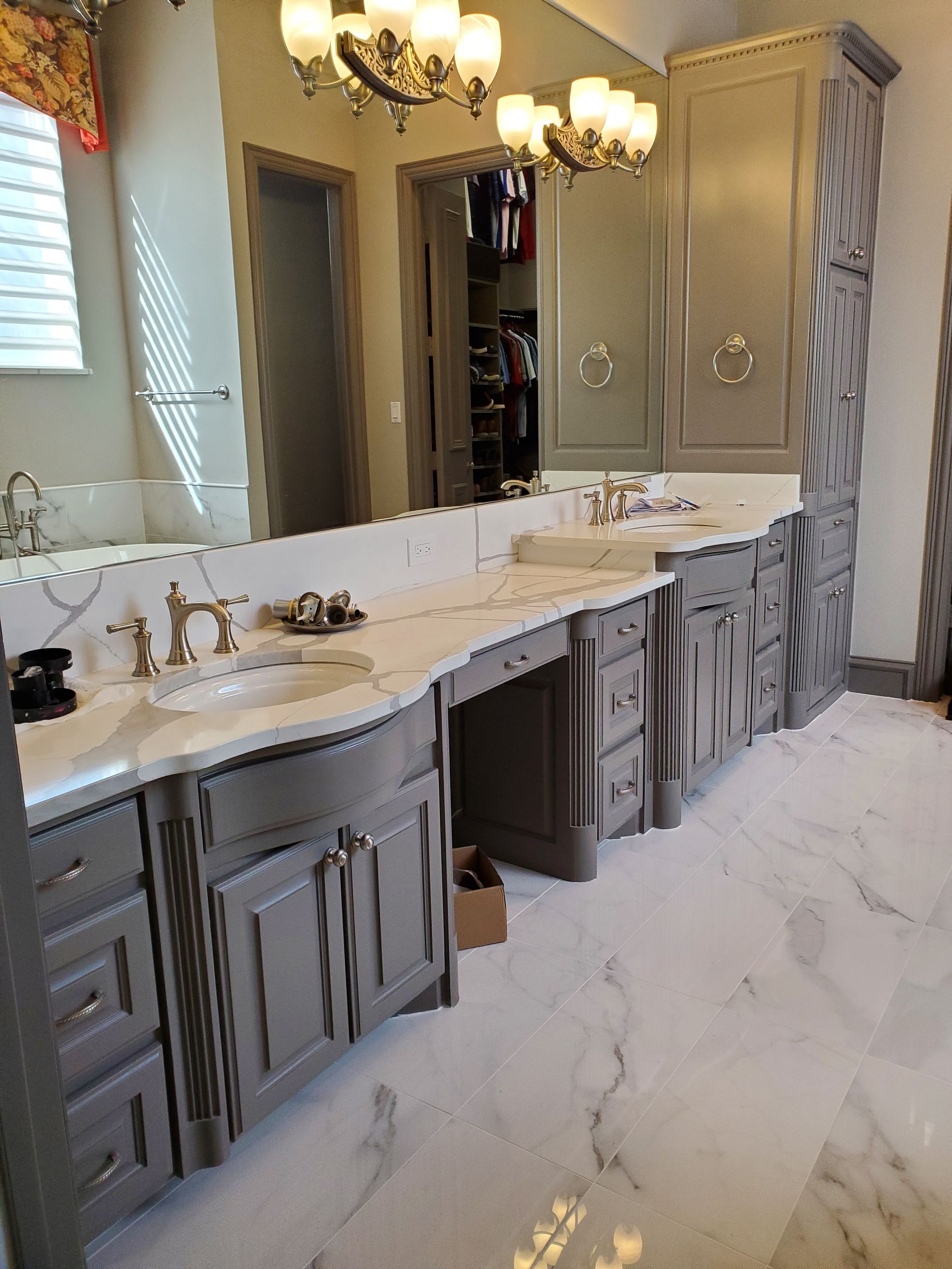 Gray bathroom vanity with marble countertop and floor, gold fixtures, and large mirror.