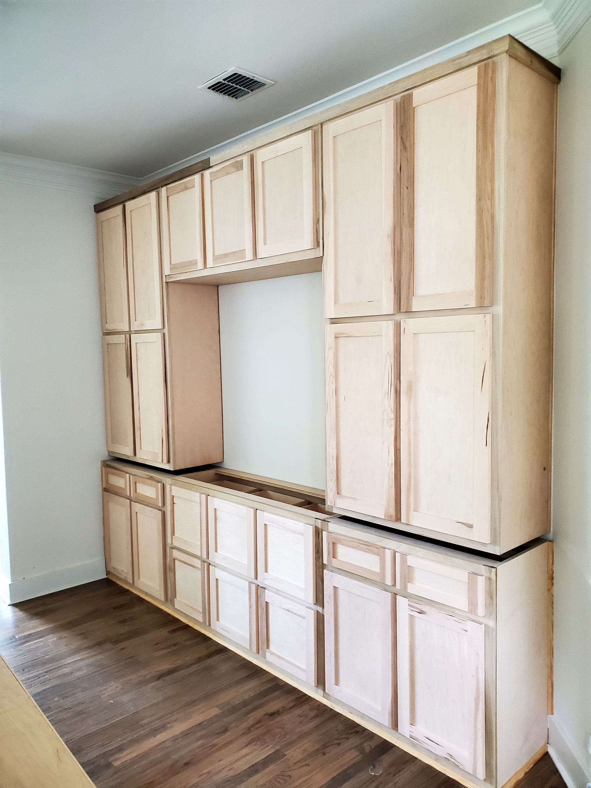 Unfinished kitchen cabinets installed on a wall, with an empty space in the middle.