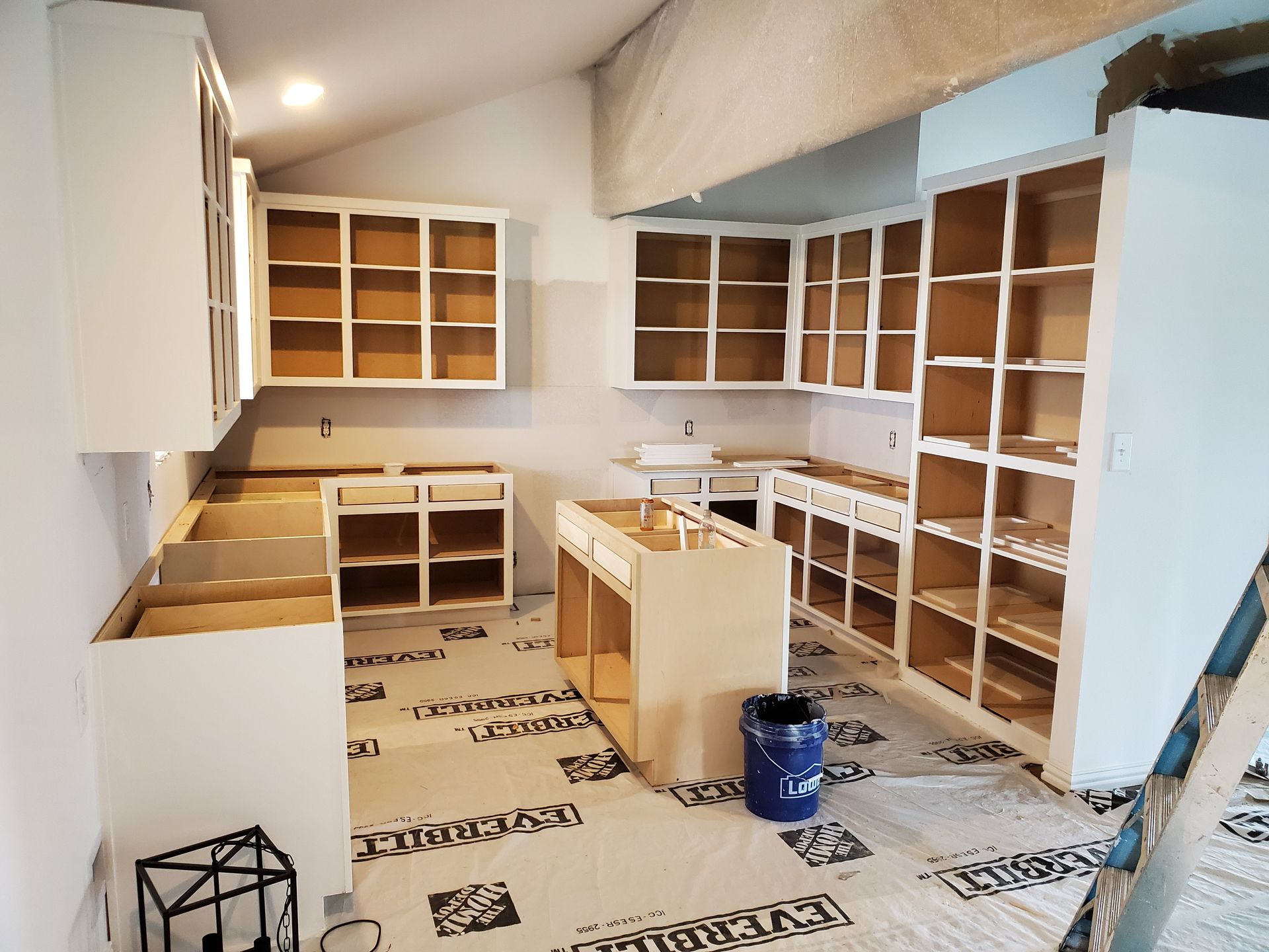 Kitchen with white cabinets under construction, light brown interior, on a protective floor covering.