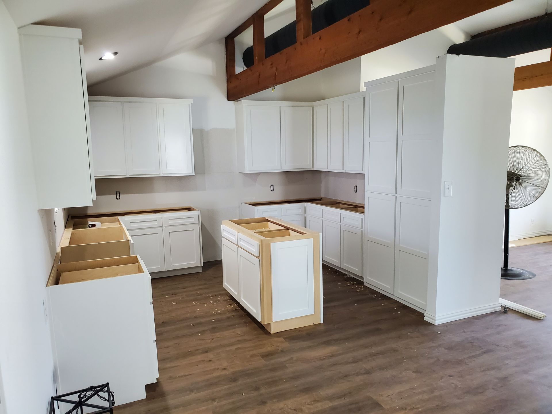White kitchen cabinets in a room with wood beams and new flooring.