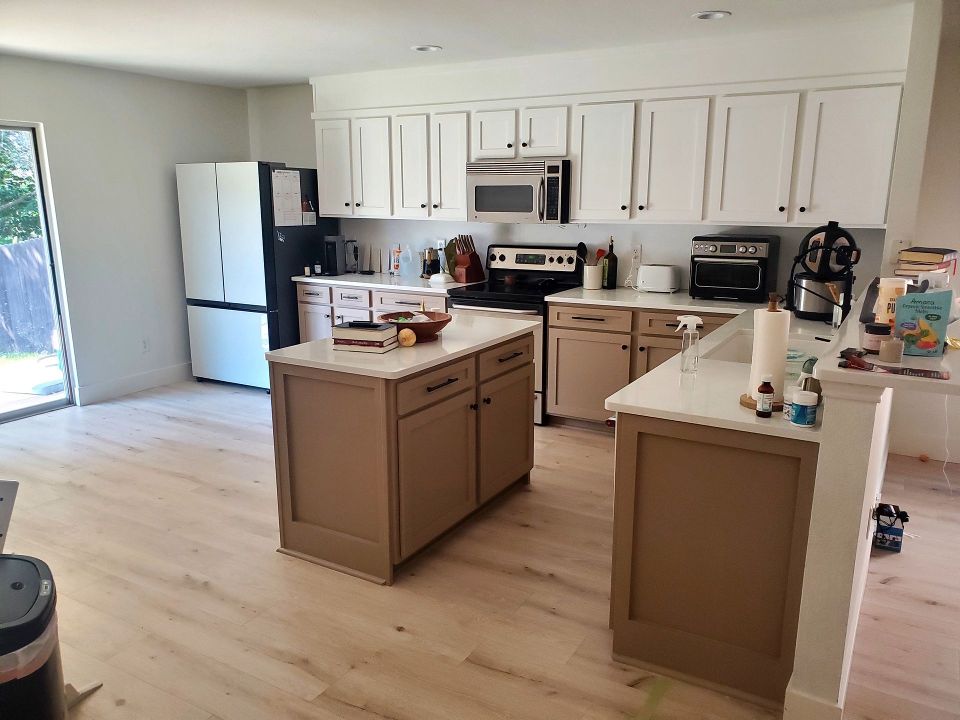 Modern kitchen with white upper cabinets, brown lower cabinets and islands, stainless appliances, light wood floors.