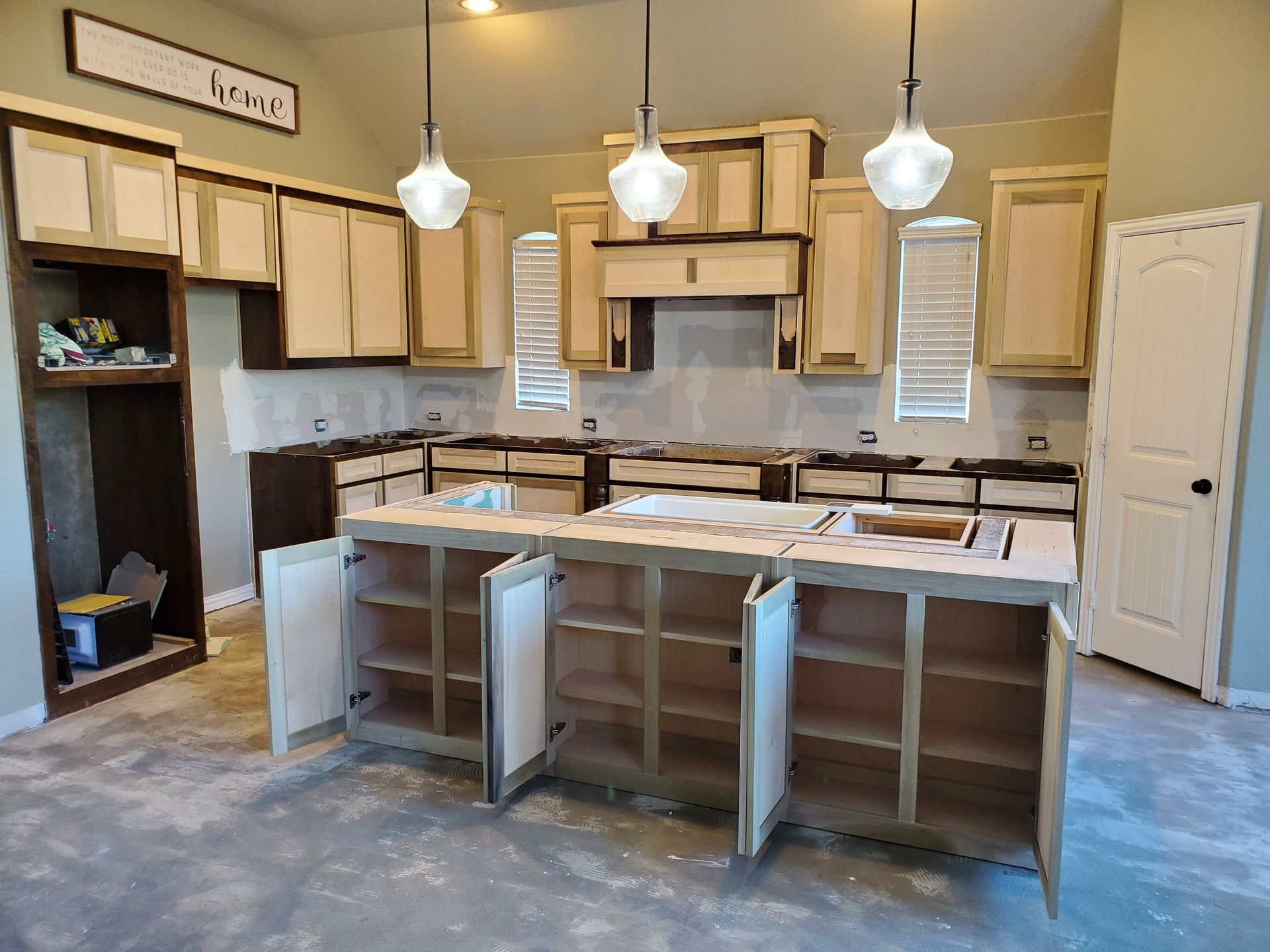 Kitchen under construction with light cabinets, island, and pendant lights.