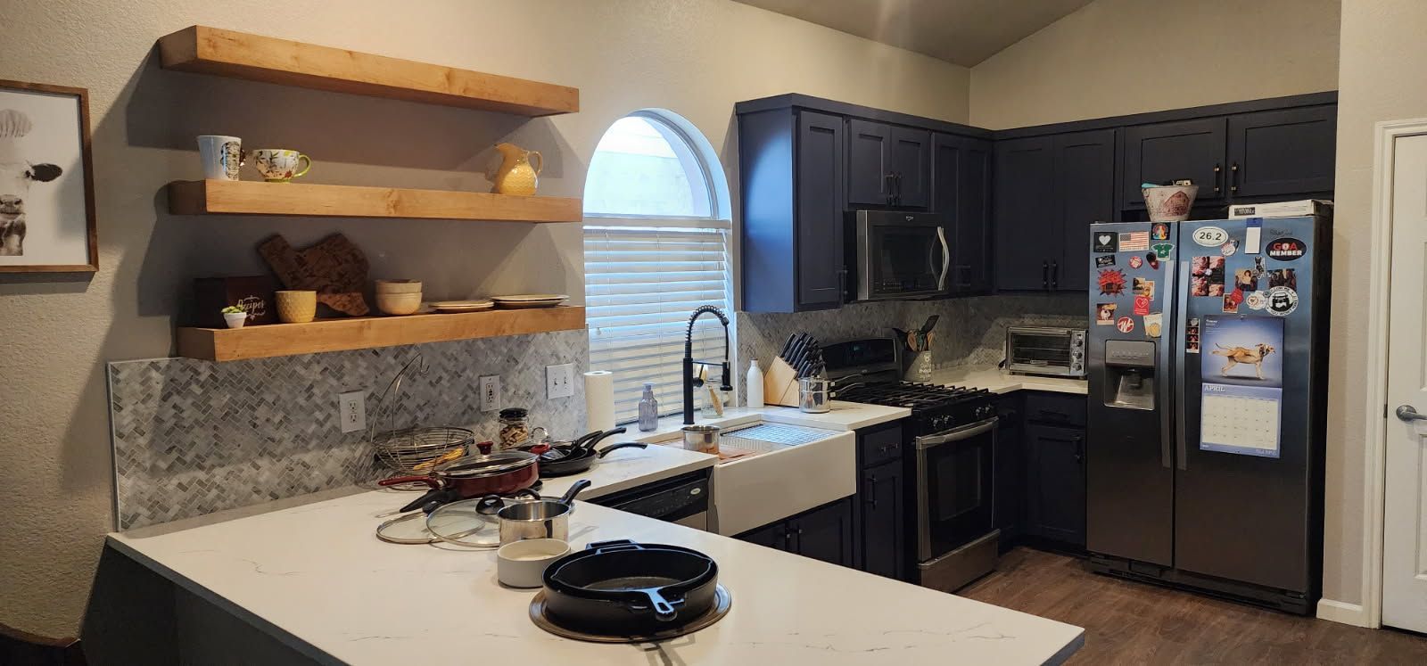 Kitchen with blue cabinets, open wooden shelves, and a stainless steel refrigerator.