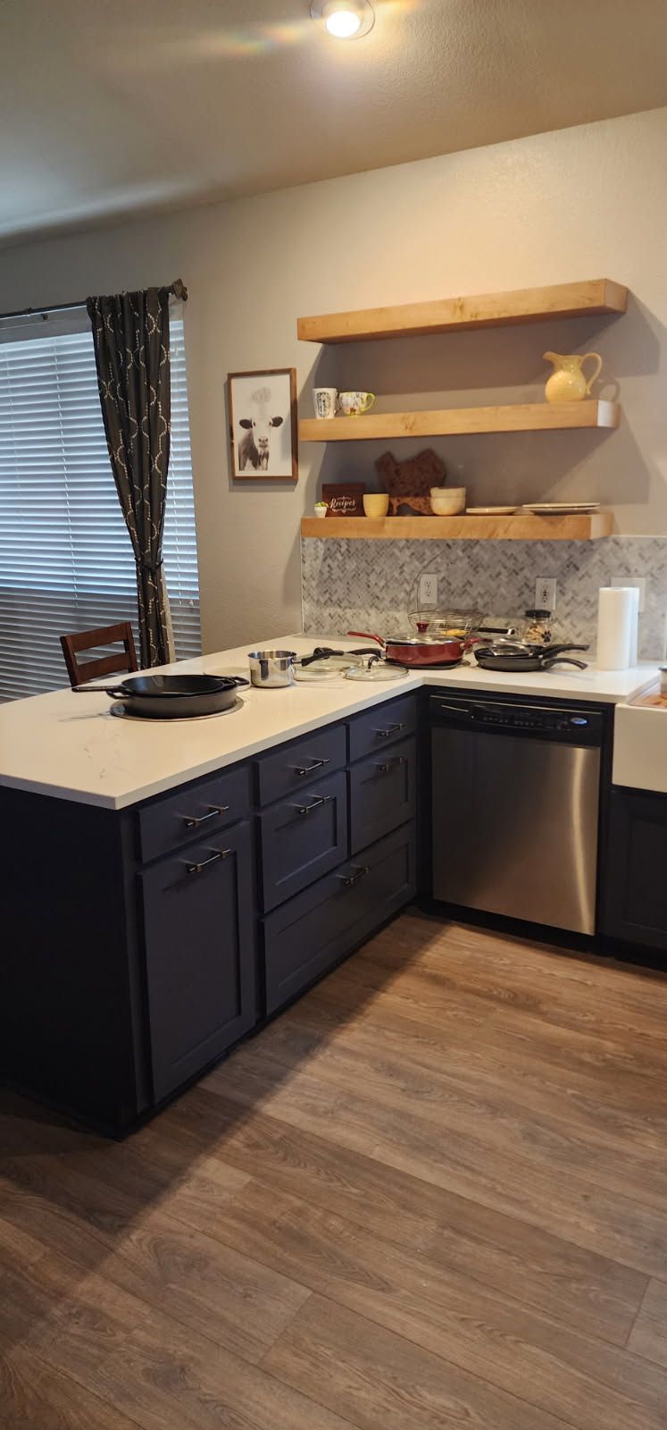 Kitchen with blue cabinets, white countertops, stainless steel appliances, and wooden shelves.