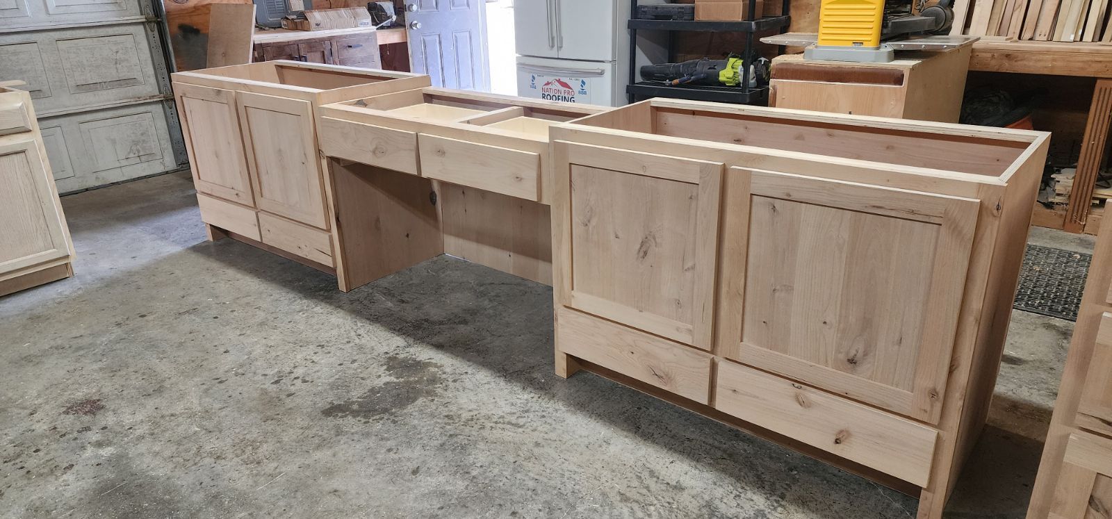 Wooden kitchen cabinets in a workshop setting. Cabinets are unfinished and awaiting hardware.