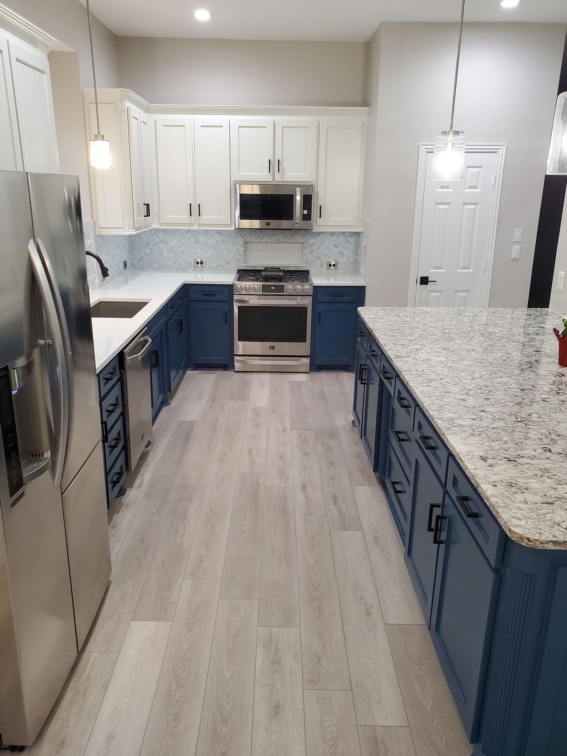 Modern kitchen with white and blue cabinets, stainless steel appliances, and a large island.