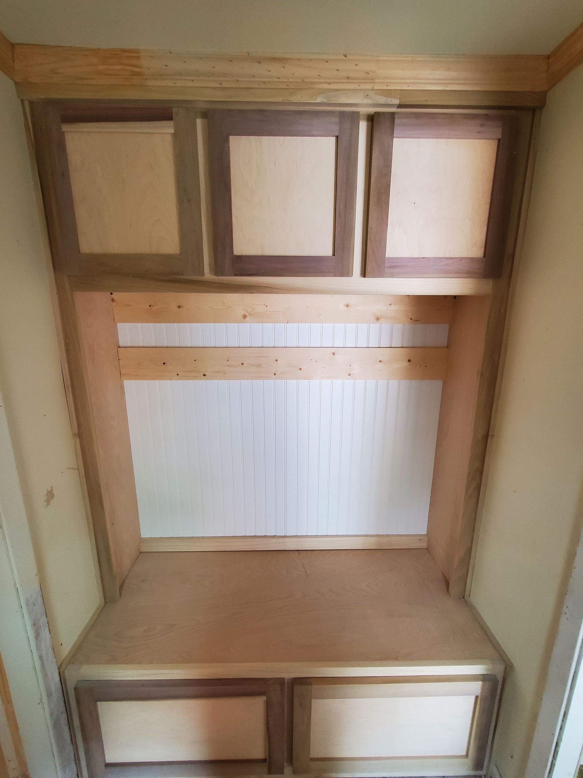 Built-in wooden cabinet with three upper doors, two lower drawers, and a bench; light brown and beige.
