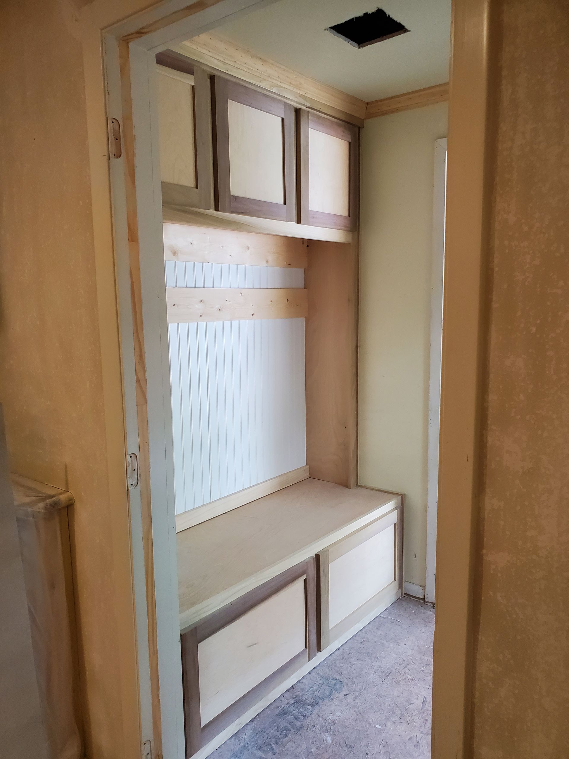 Built-in entryway bench and storage cabinets in a light-colored wood, under construction.
