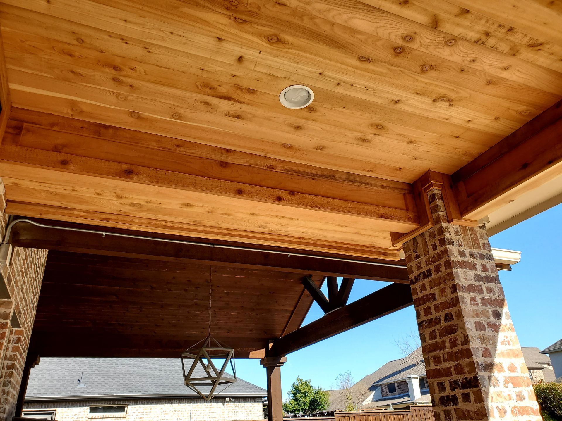 Wooden porch ceiling with recessed light, supported by brick columns and wooden beams.