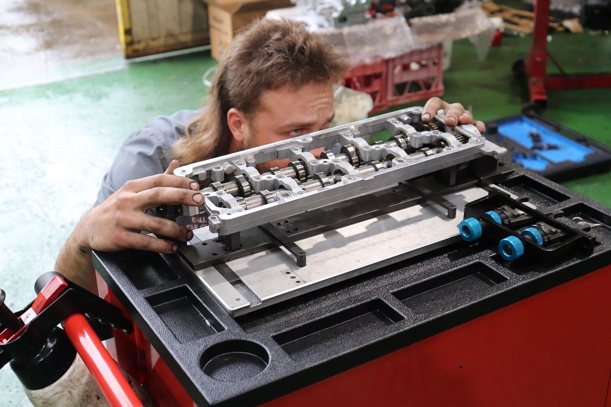 Man With Mullet Inspecting Engine Part On Workbench — Ballina Car Centre in Ballina, NSW