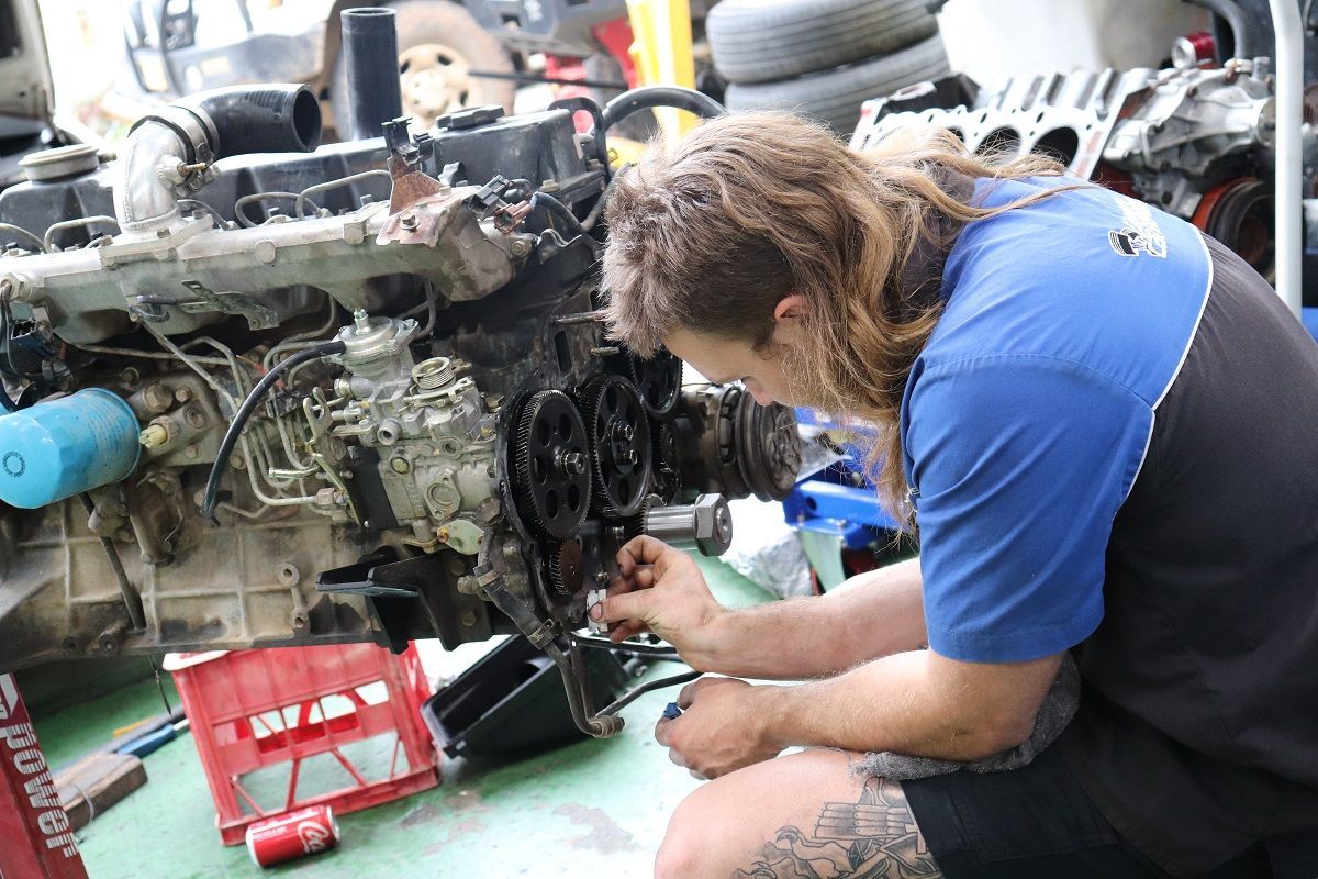 Mechanic Working On Car Engine Kneeling In Garage — Ballina Car Centre in Ballina, NSW