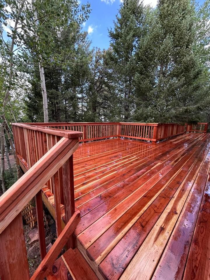 A large wooden deck with stairs leading up to it surrounded by trees.