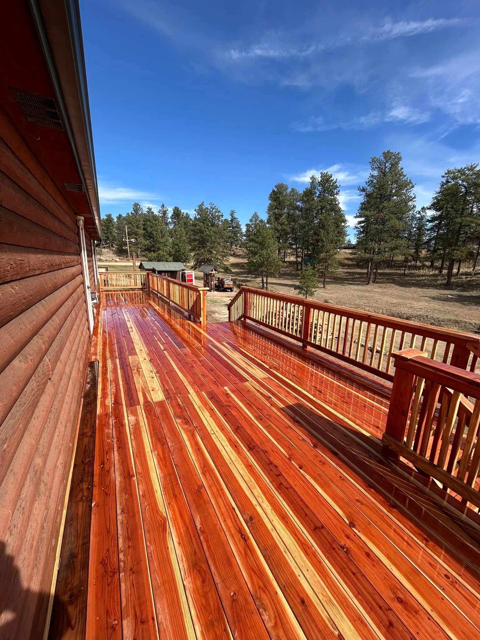 A large wooden deck with a railing and trees in the background.