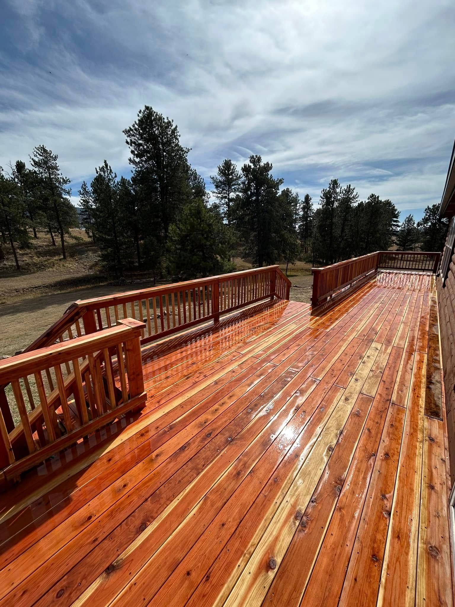 A large wooden deck with a railing and trees in the background.