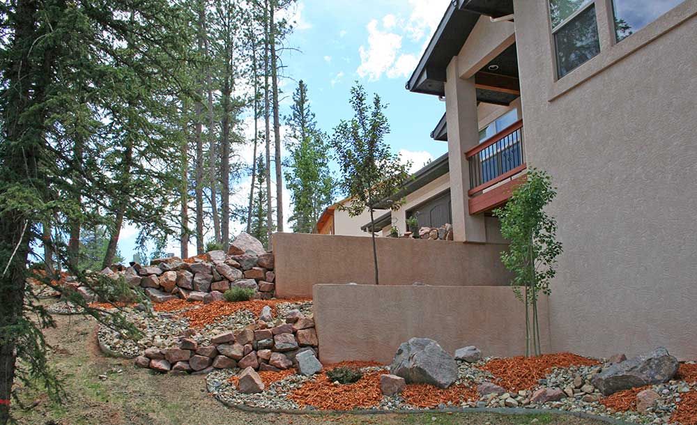 A house with a balcony is surrounded by trees and rocks