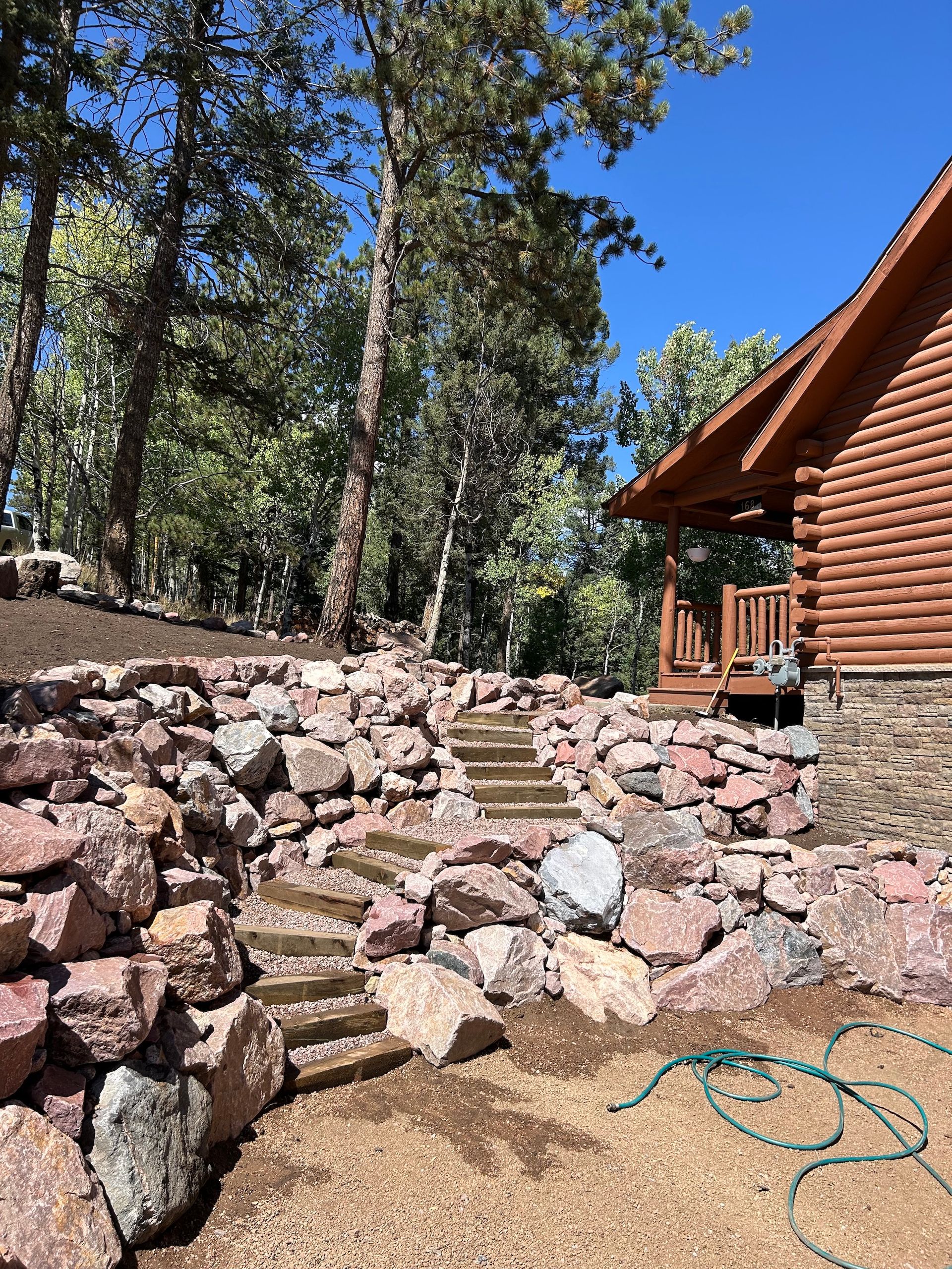A log cabin with stairs leading up to it is surrounded by rocks and trees.