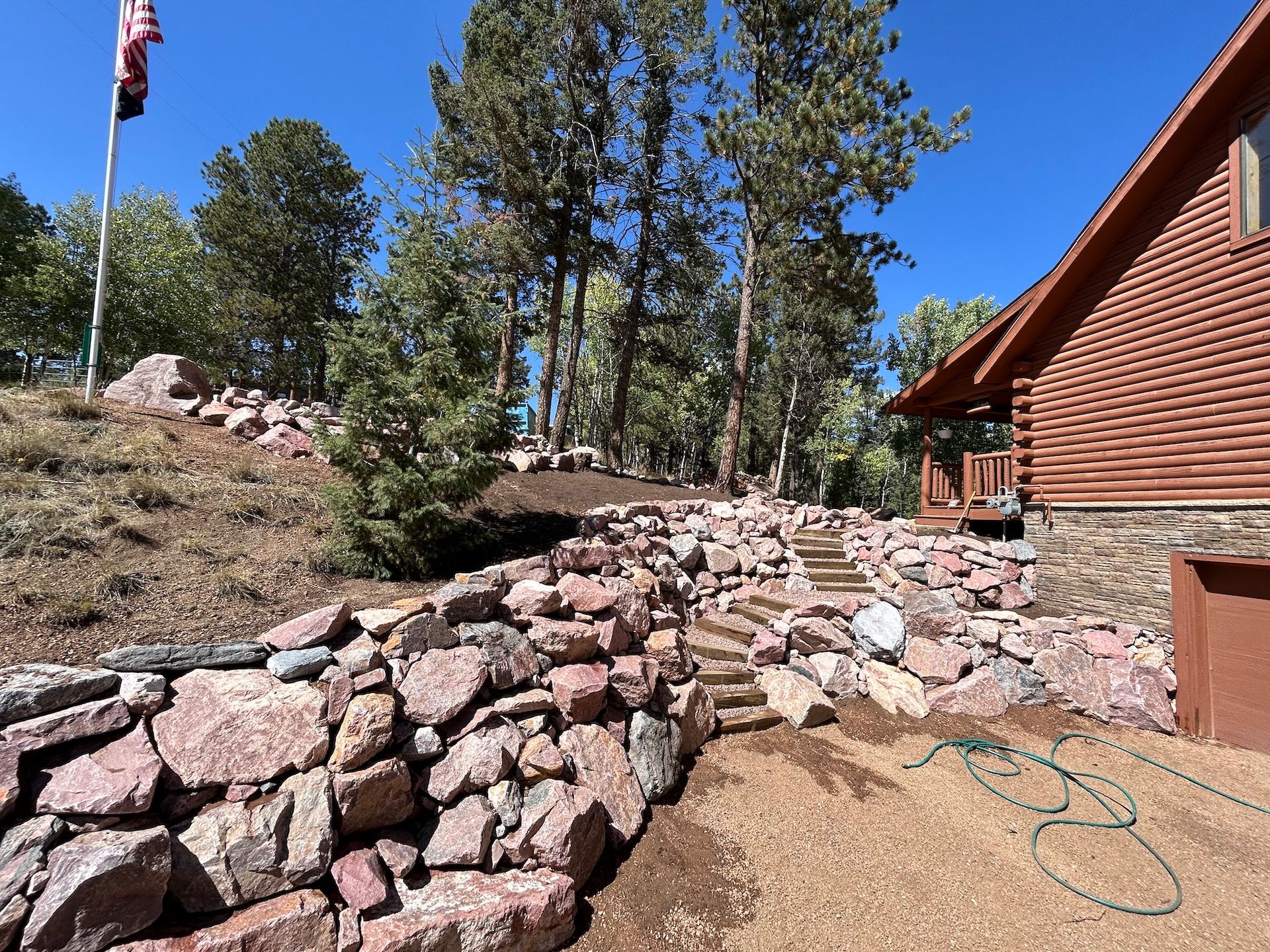 A large rock wall is in front of a log cabin.