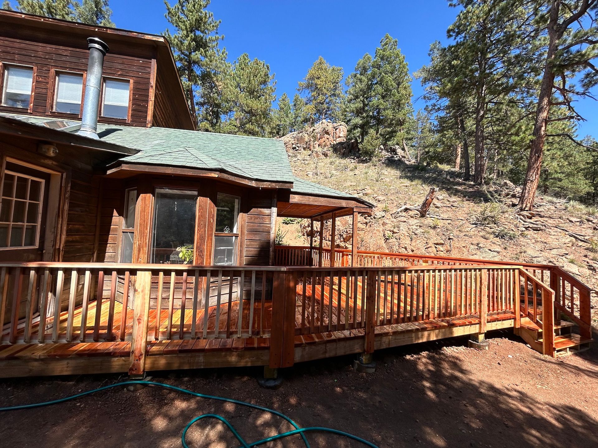 A wooden house with a large deck in front of it surrounded by trees.