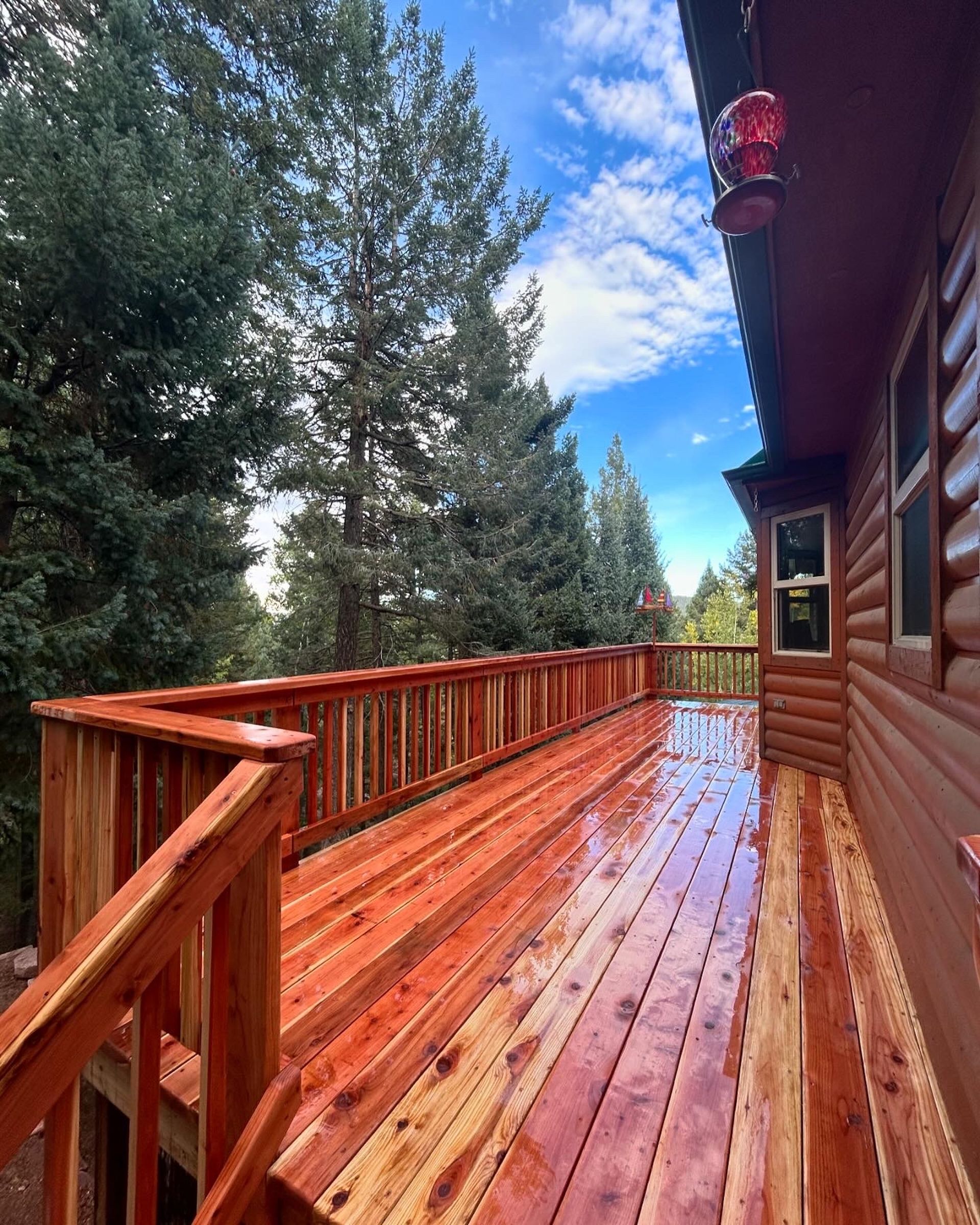 A large wooden deck on the side of a log cabin surrounded by trees.