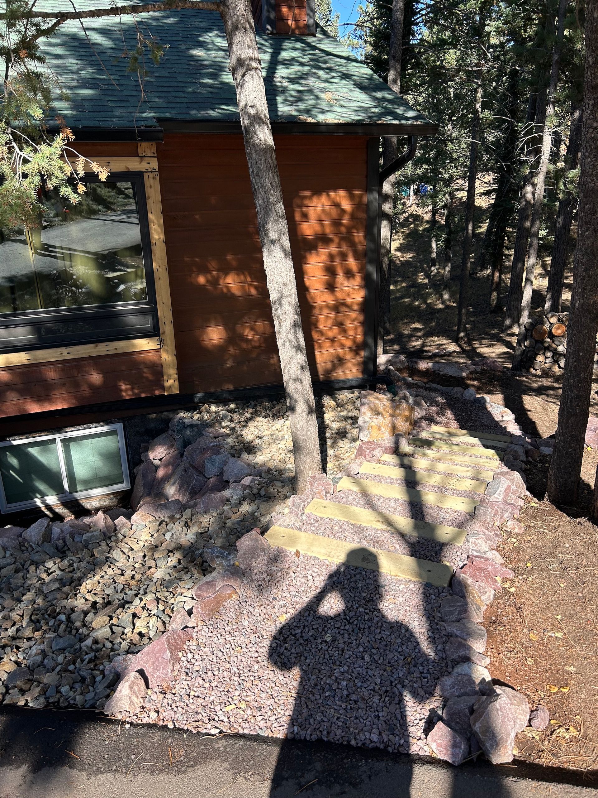 A shadow of a person standing in front of a house in the woods.